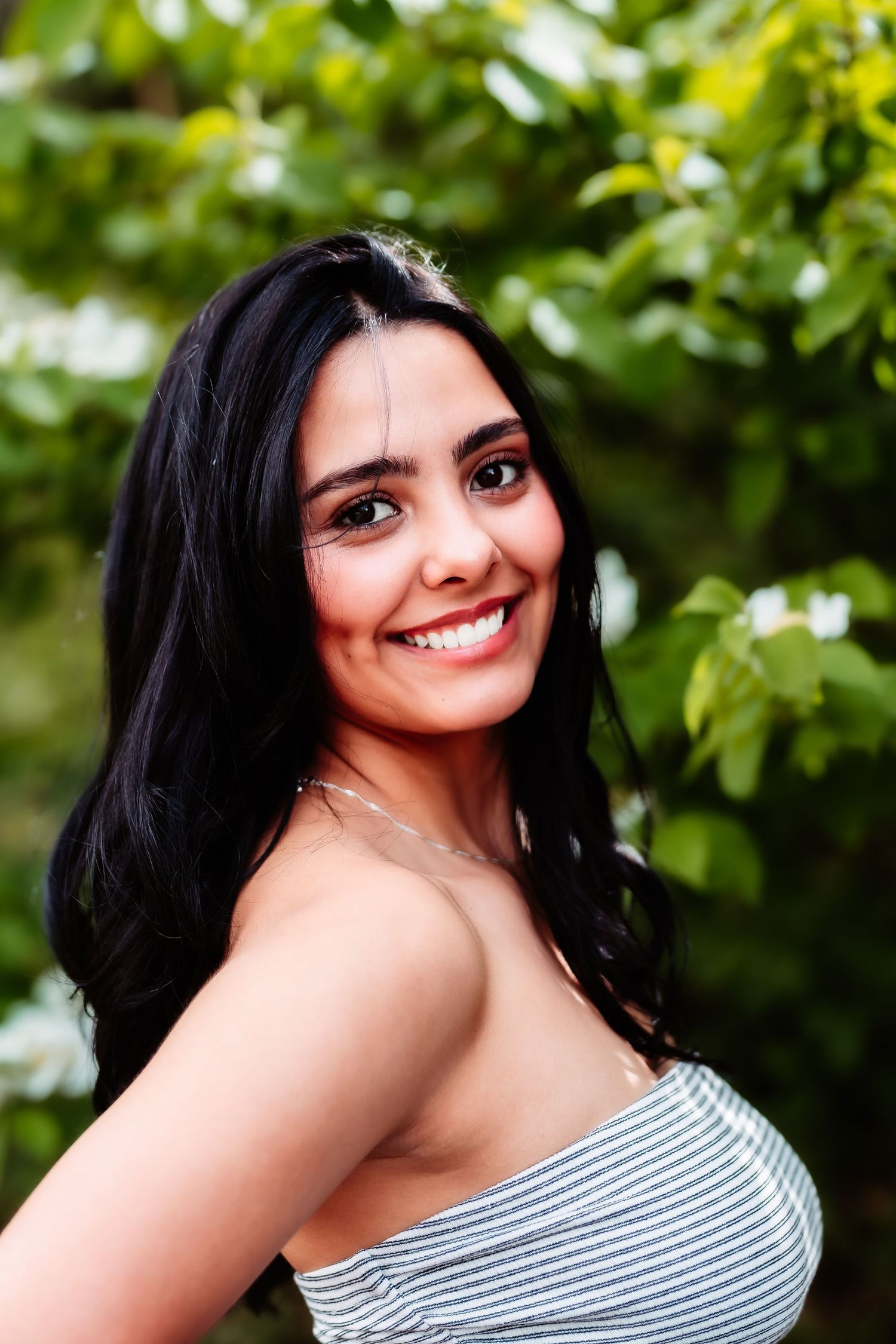 A portrait of someone in a striped top smiling outdoors with green foliage in the background.