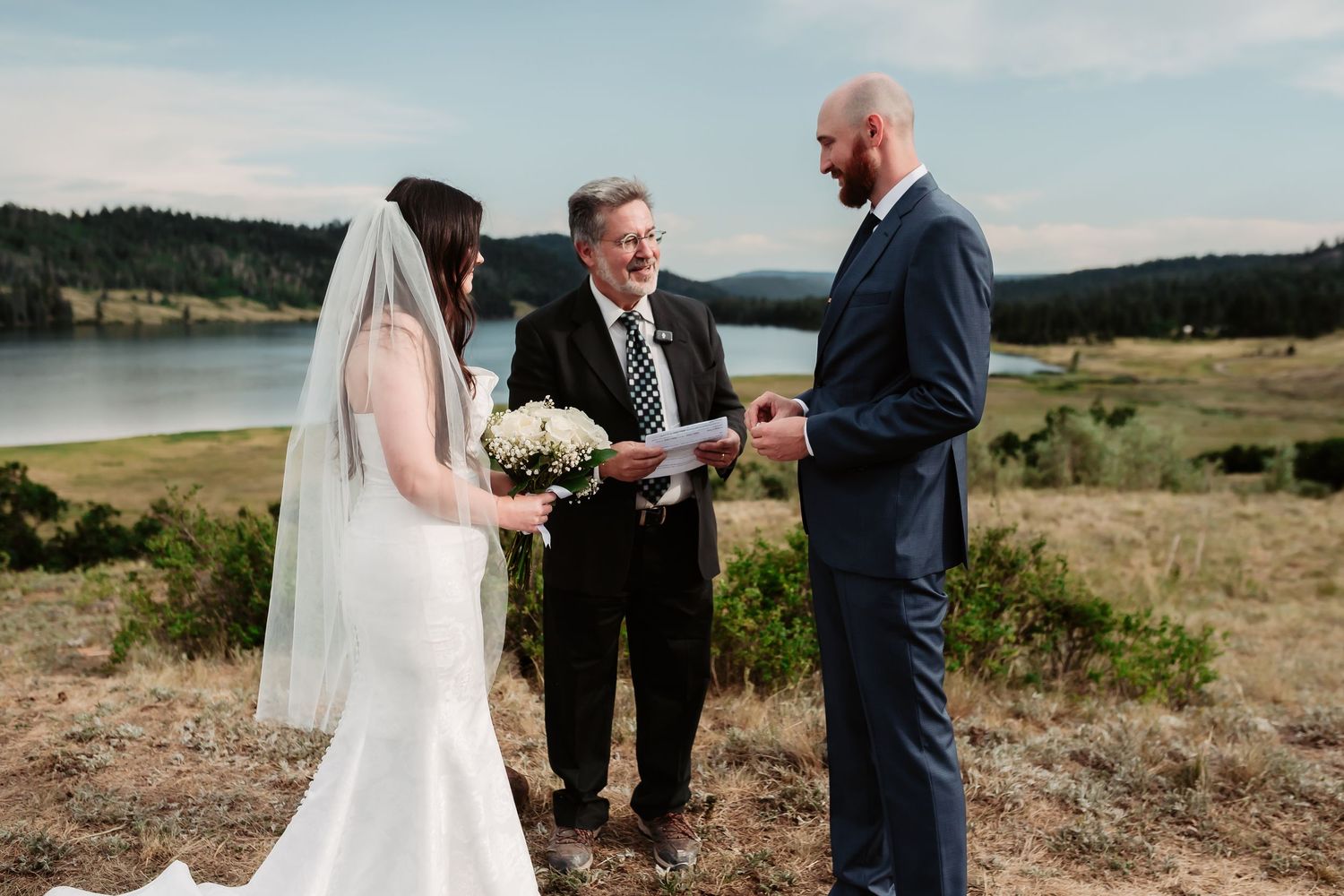 A wedding ceremony takes place on a hilltop overlooking a scenic mountain lake.