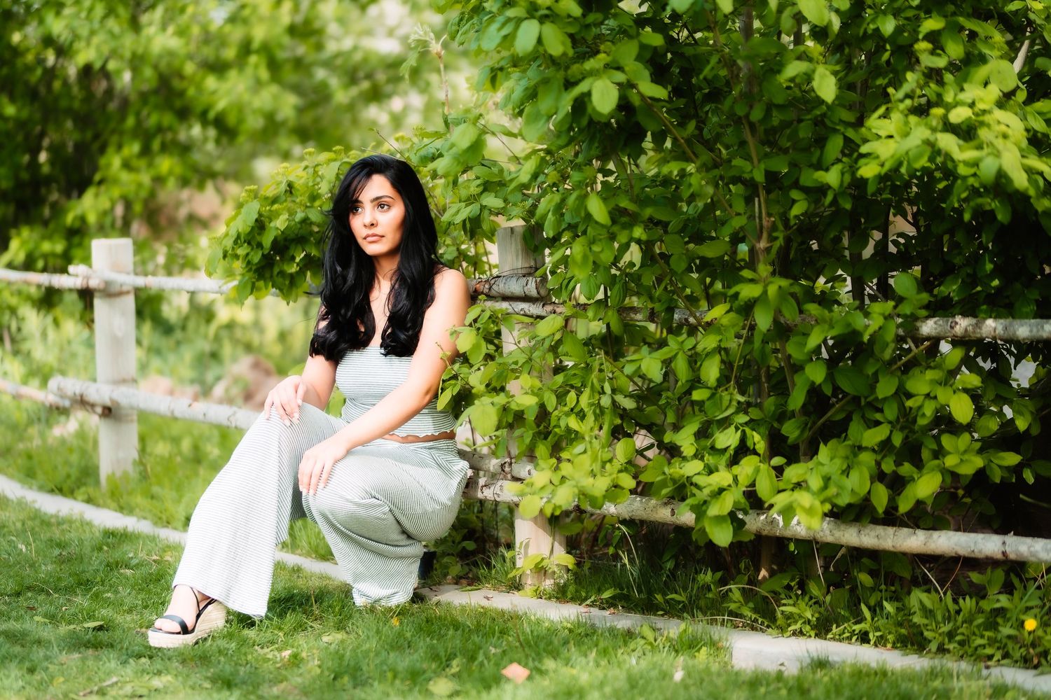 Casual outdoor portrait in a garden setting with white fence and lush greenery.