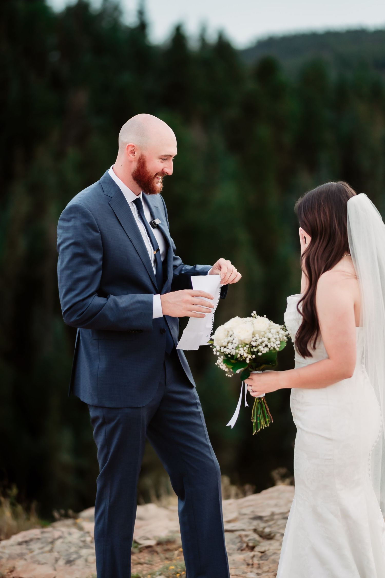 Wedding couple shares moment during mountain ceremony with white floral bouquet.