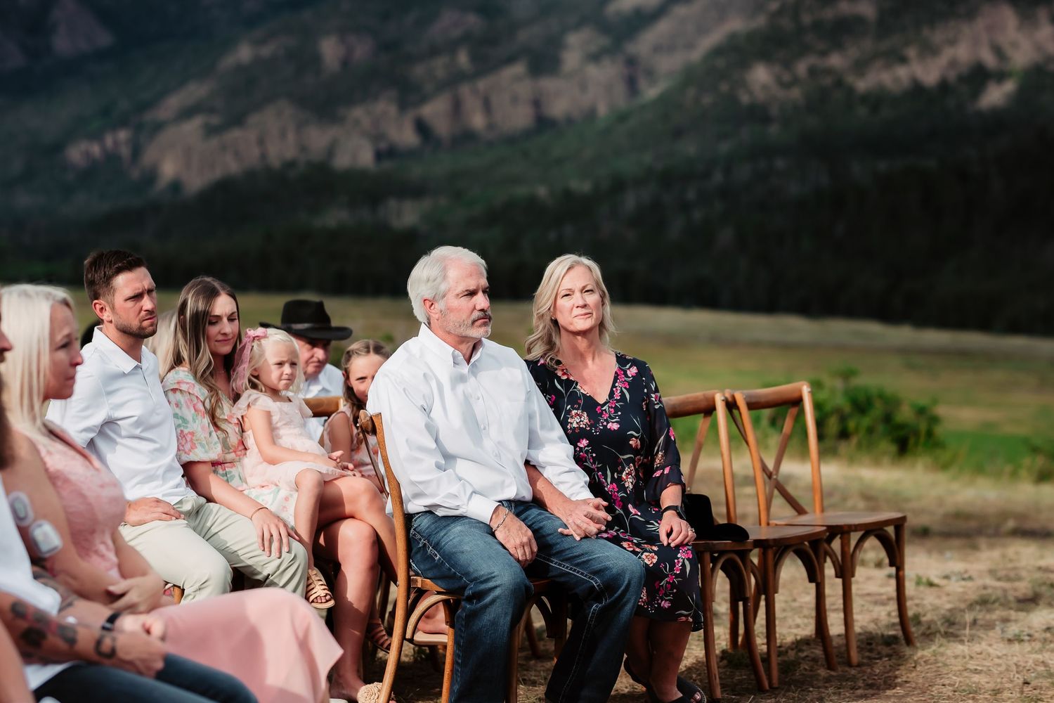 Rustic wooden chairs line up at an outdoor wedding venue with mountain views.