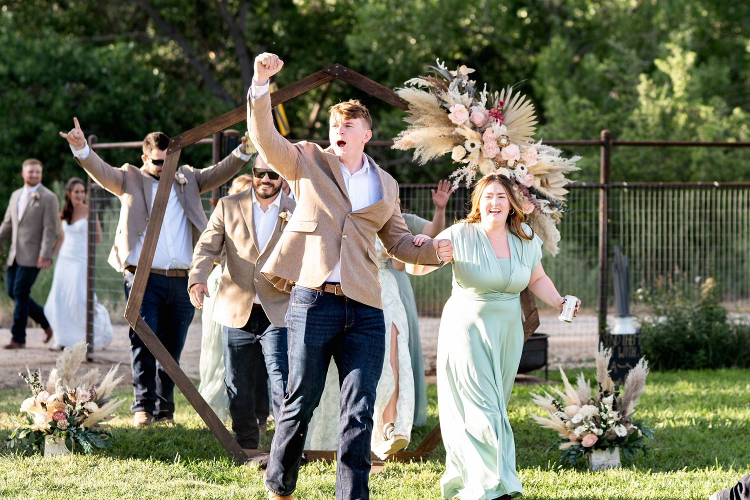 Newlyweds celebrate with raised arms while walking through a garden setting with dried floral decorations.