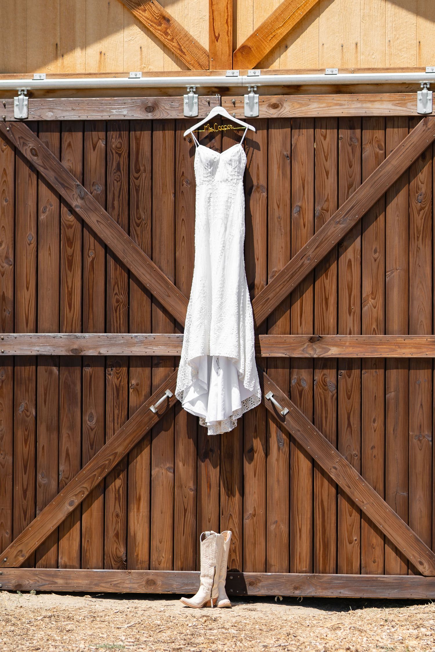 White wedding dress hanging on wooden barn door with cowboy boots placed beneath it.