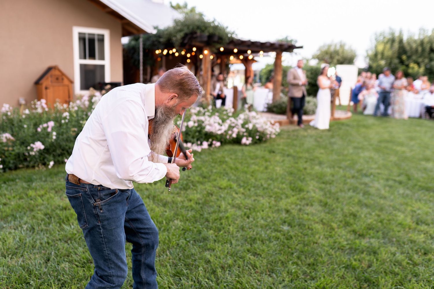 Guest takes photos at an outdoor wedding reception with twinkling lights and flower gardens.
