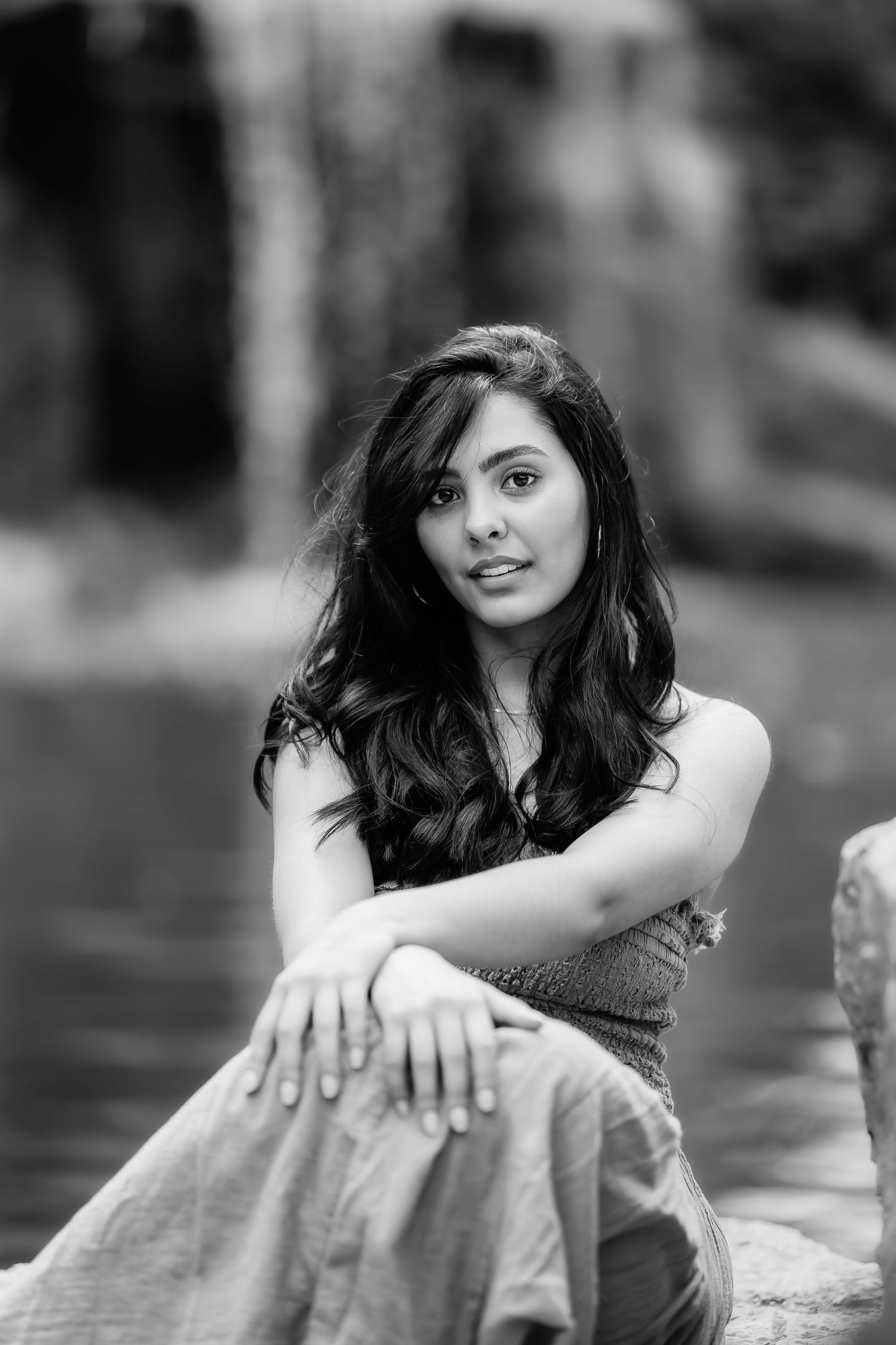 Artistic black and white portrait showing a person in casual attire seated on rocks outdoors.