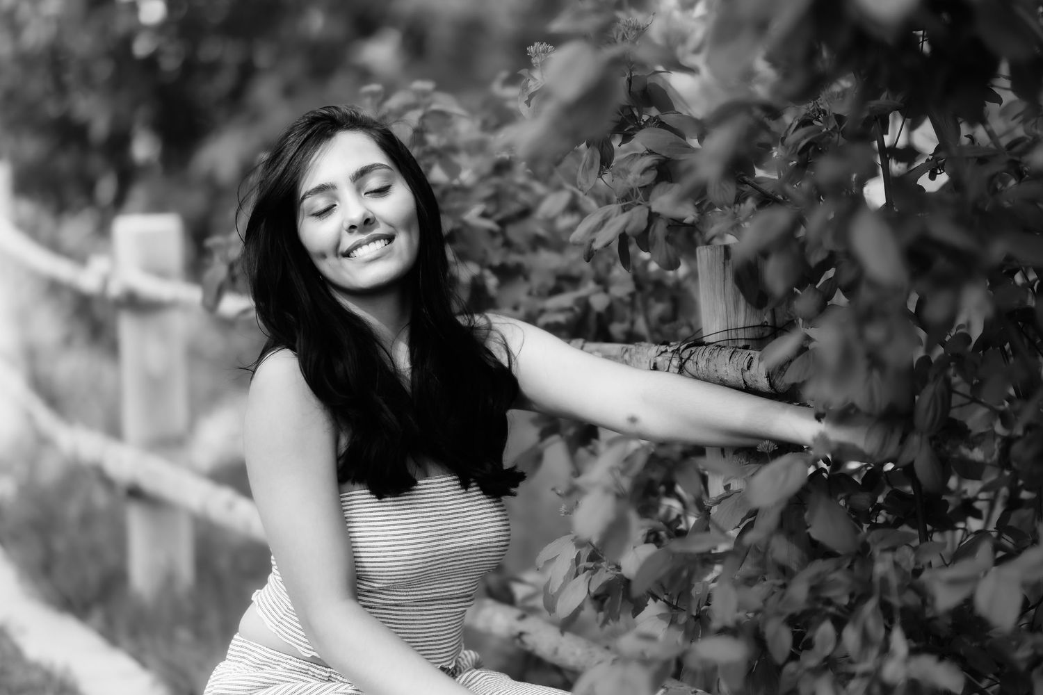 A black and white outdoor portrait showing a joyful expression among leaves.