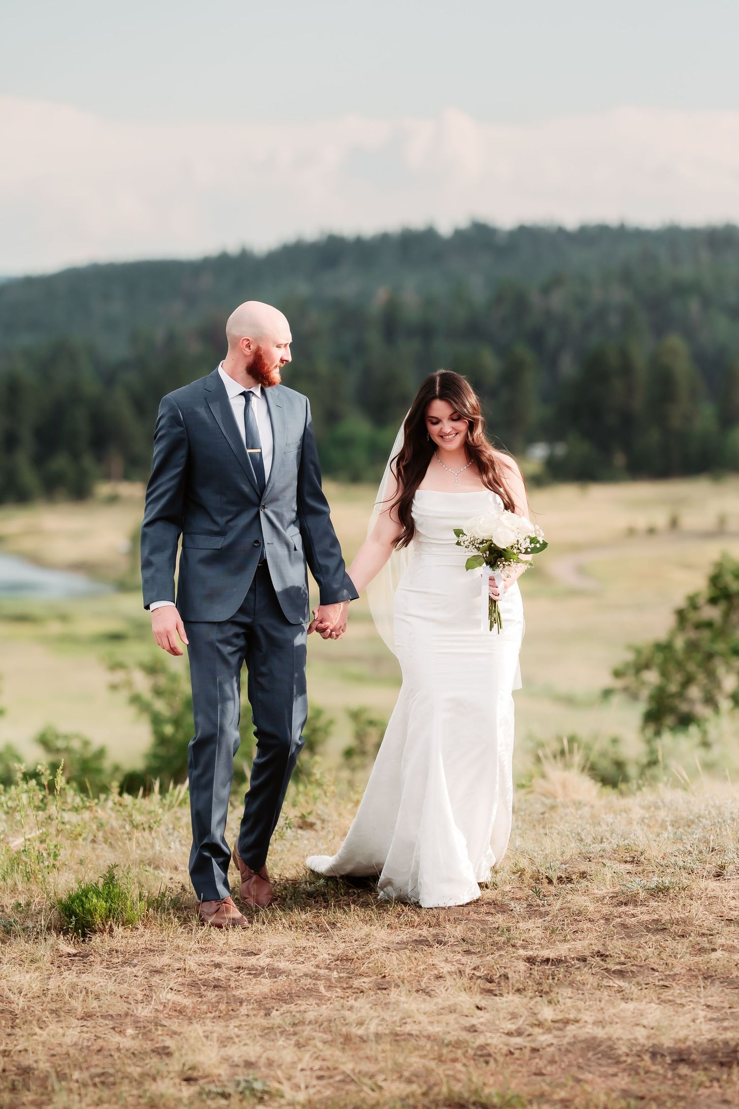 A couple walks hand in hand on a mountain trail during their wedding photo session.