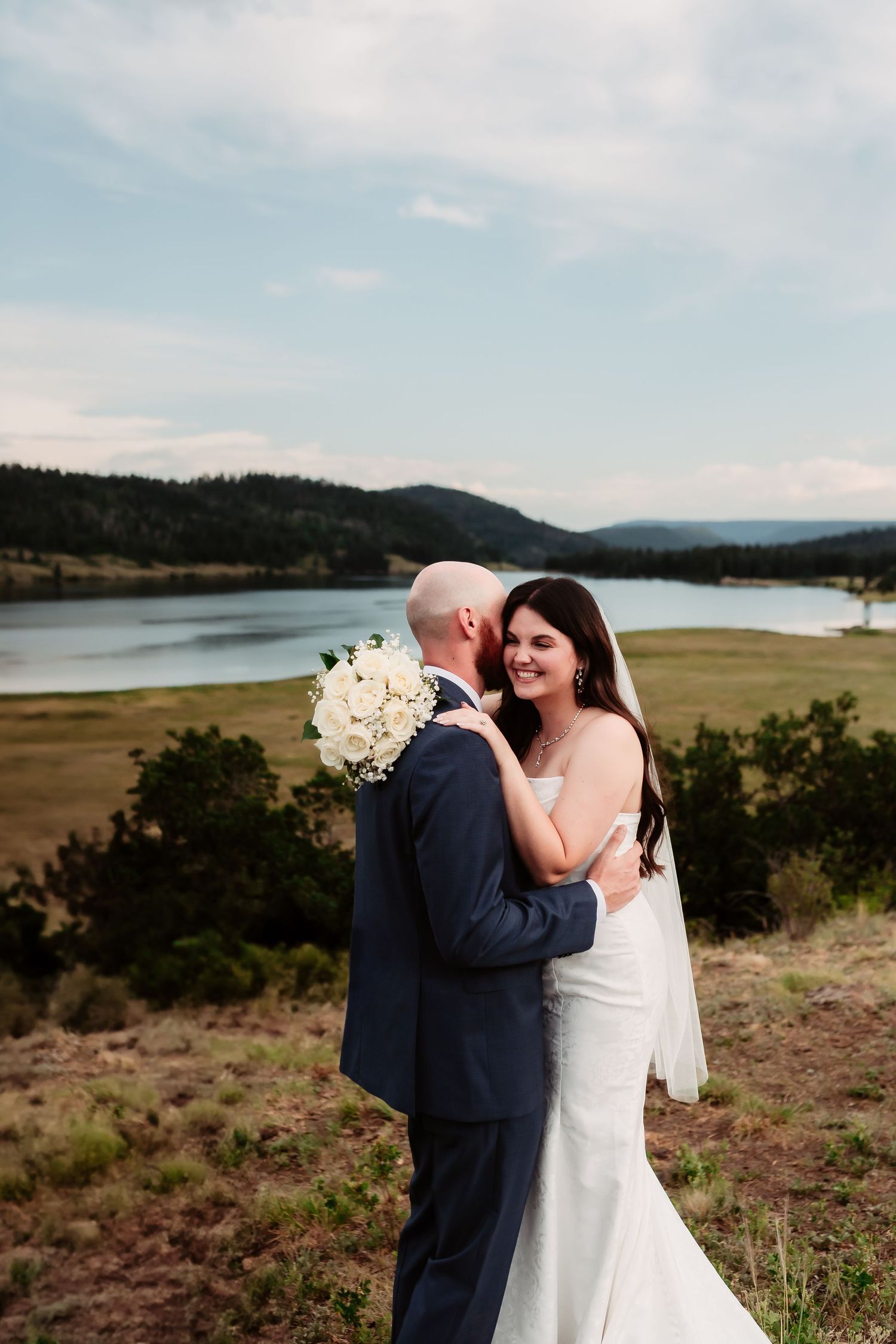 A couple embraces during their wedding photoshoot with a stunning mountain lake backdrop.