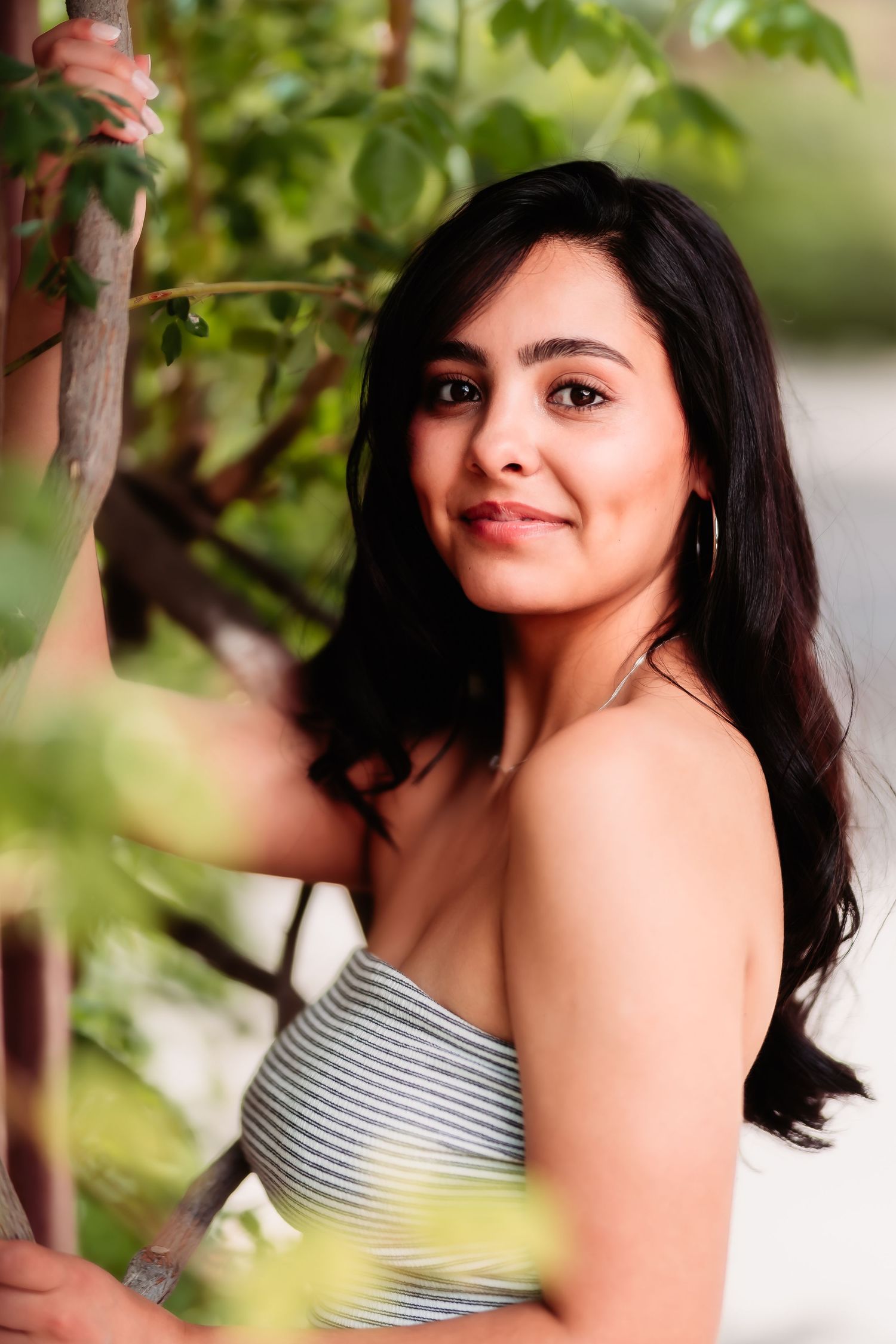 Natural outdoor portrait with striped top framed by green leaves and soft lighting.