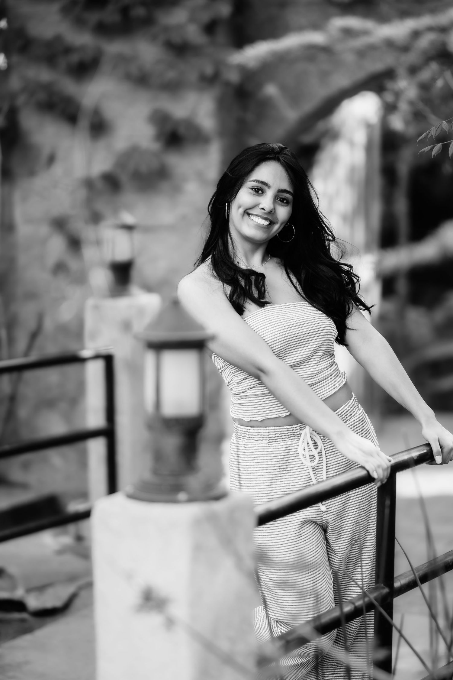 A black and white portrait of someone in casual wear leaning against a metal railing.