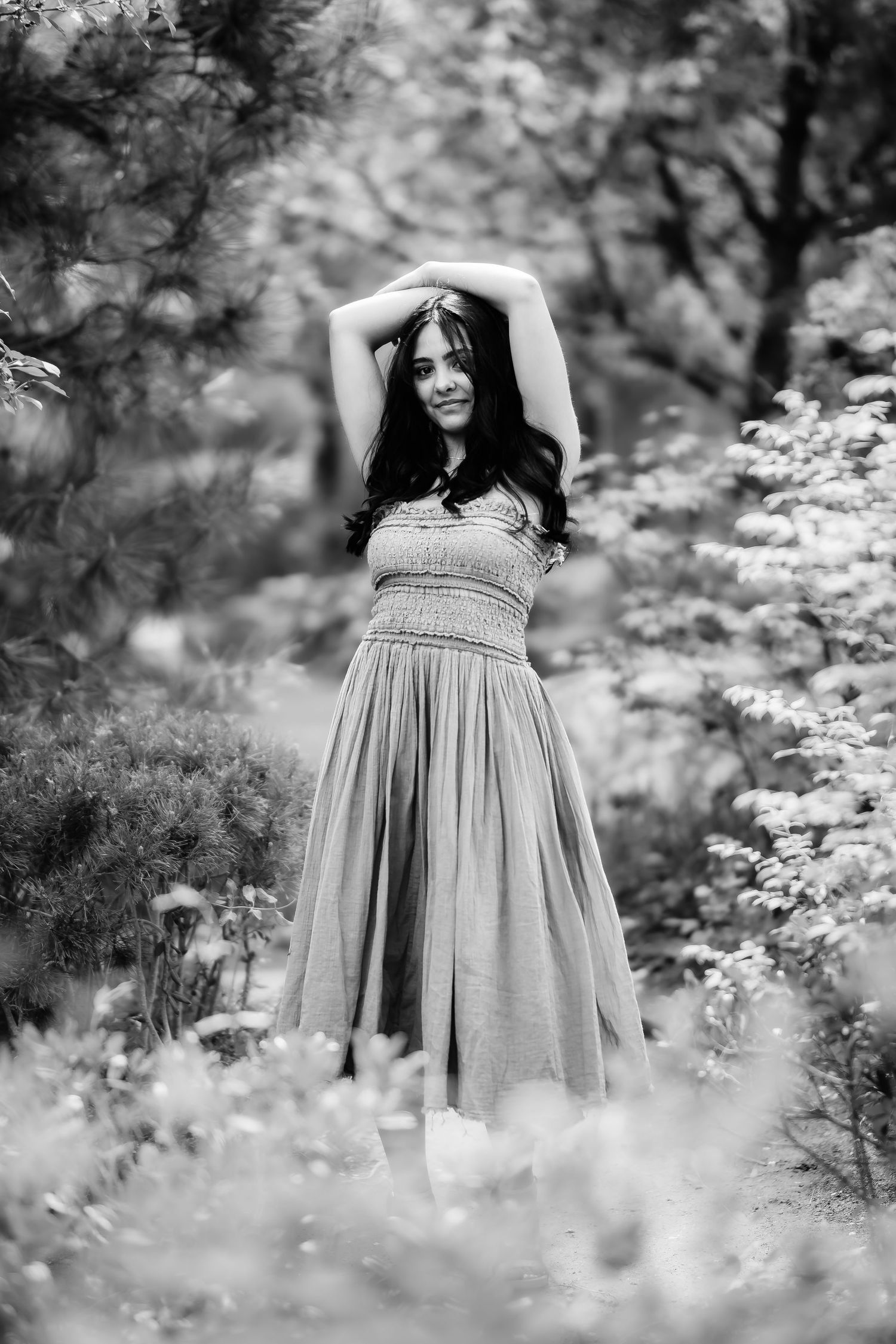 Black and white photo of a person in a flowing dress posing gracefully in a garden setting.