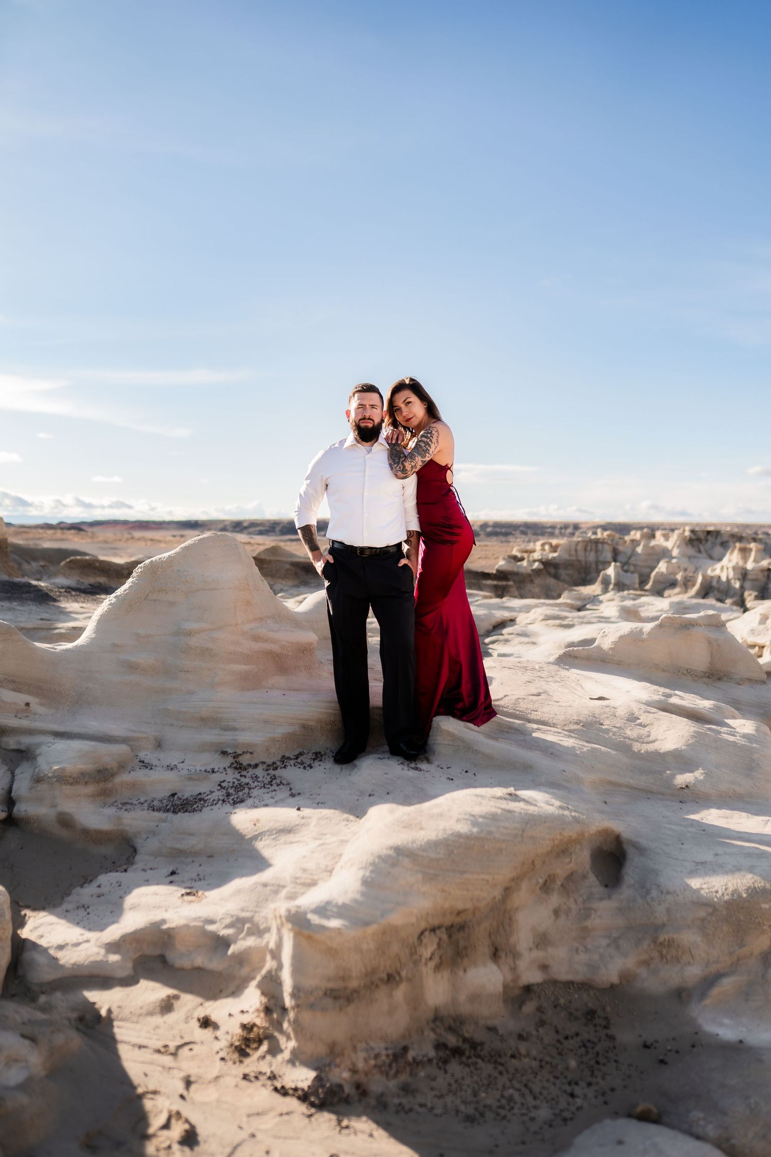 A couple poses together on white rock formations in a desert landscape under bright blue skies.