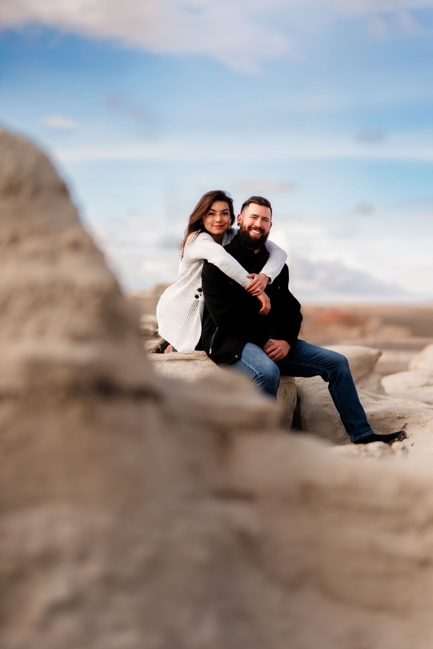 Two people share a tender embrace while sitting on rocky formations in a desert landscape.