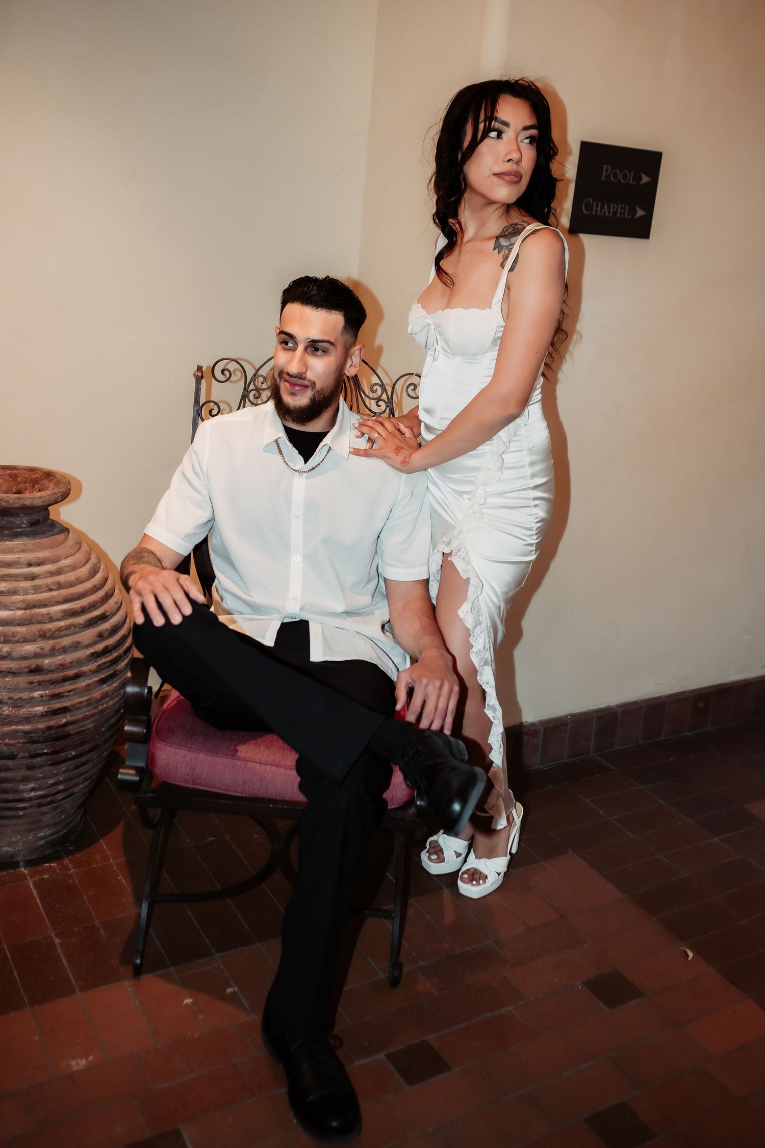 Couple in formal white attire posing together near decorative pottery and furniture.