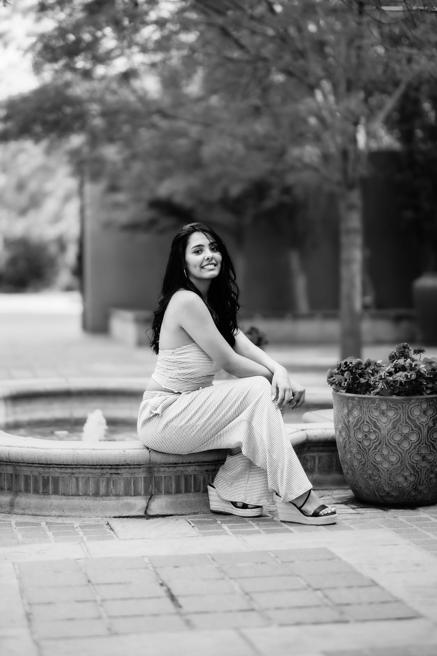 A black and white photo of someone sitting on a brick ledge near a decorative planter.