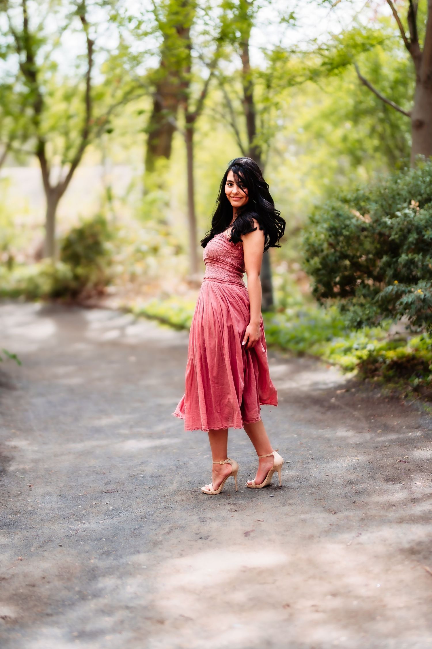 A figure in a pink sundress walks barefoot along a garden path surrounded by lush greenery.