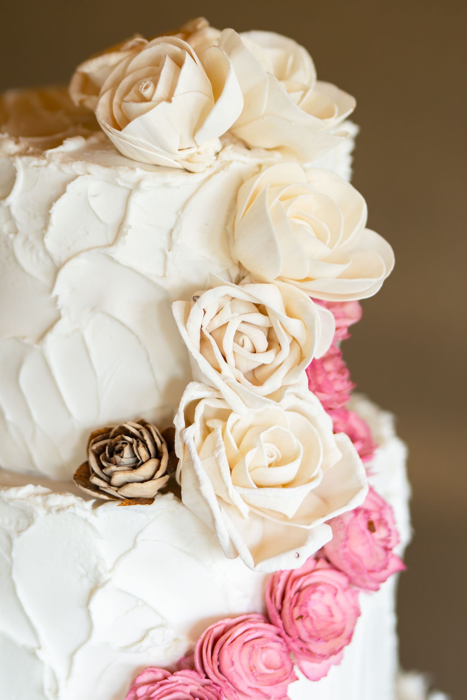 Elegant white and pink sugar roses cascade down the side of a tiered wedding cake.