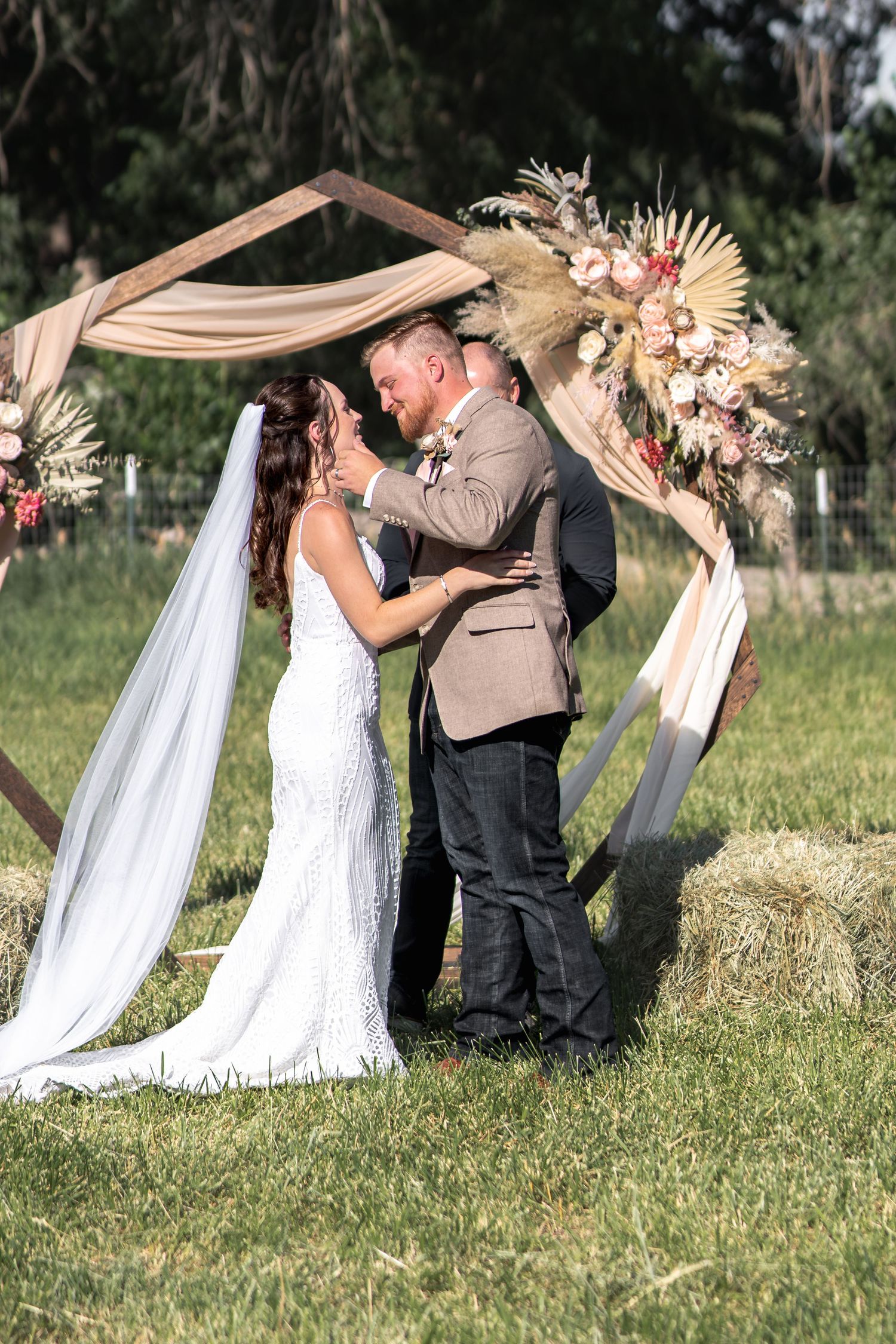 Wedding ceremony under wooden arch decorated with dried flowers and flowing fabric.
