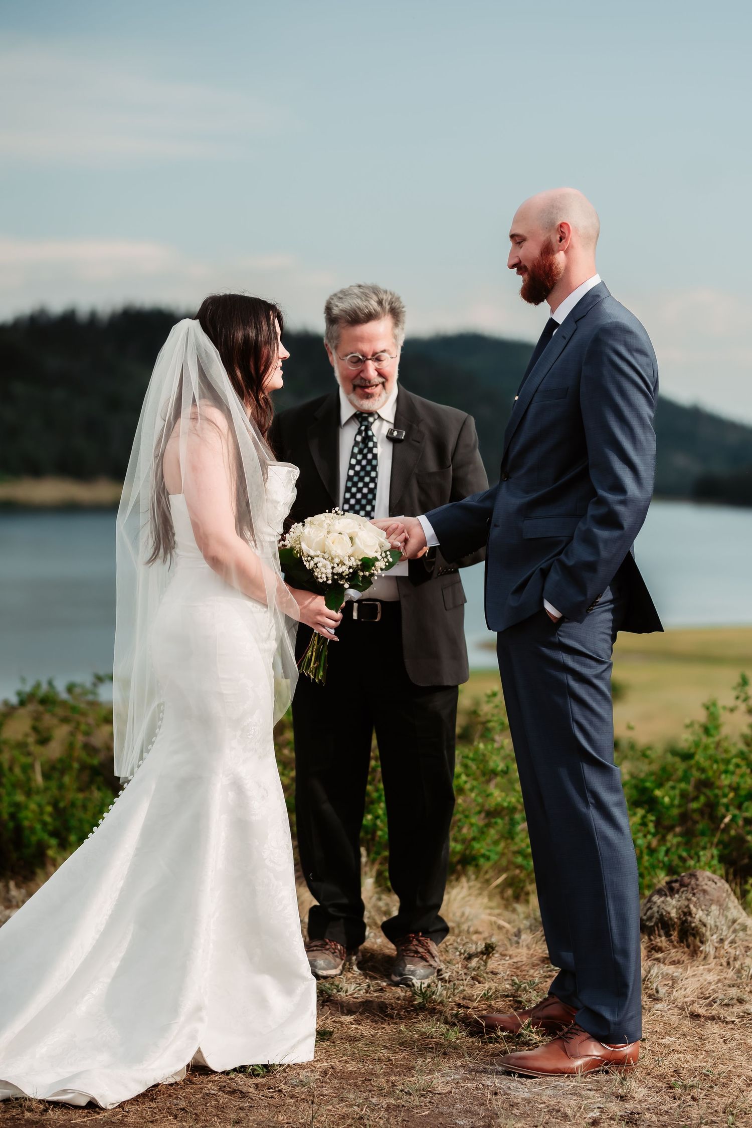 A wedding ceremony takes place on a scenic clifftop overlooking a serene lake.