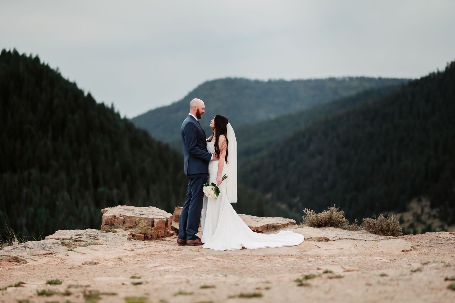 A wedding couple shares an intimate moment on a rocky mountain overlook.