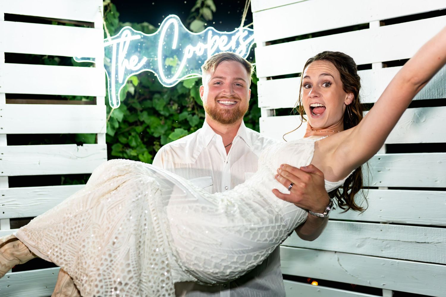 Playful newlyweds share a fun moment on a white wooden swing set.