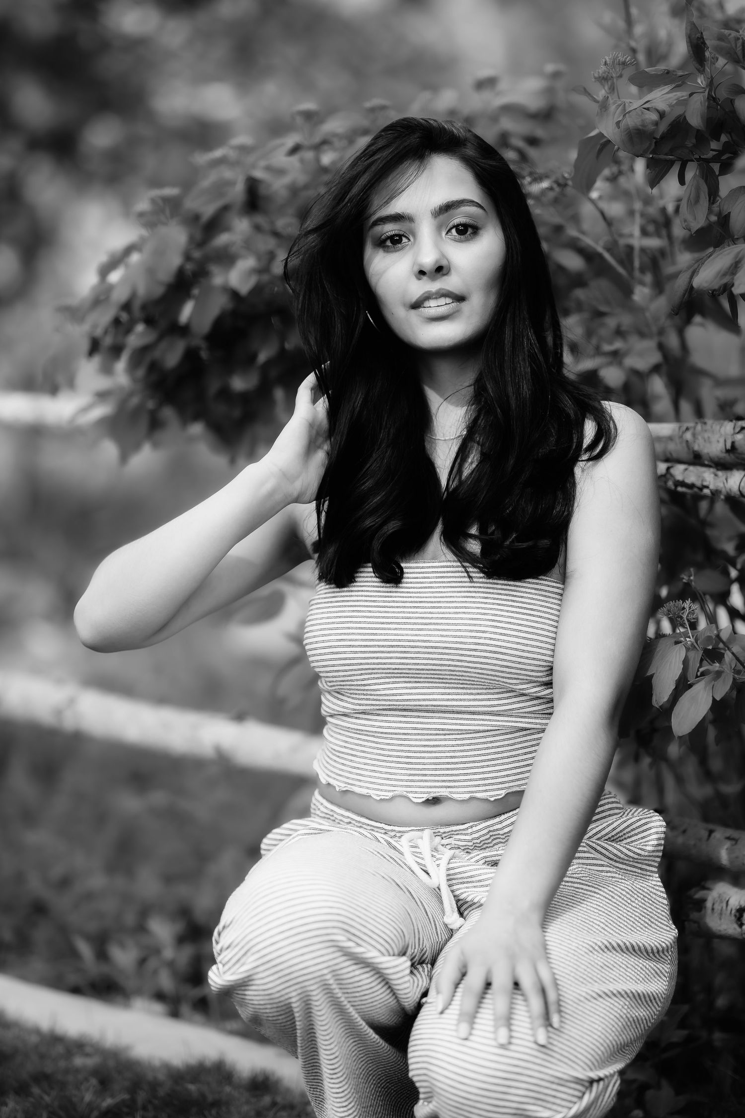A black and white photo of a woman in striped casual wear sitting outdoors.