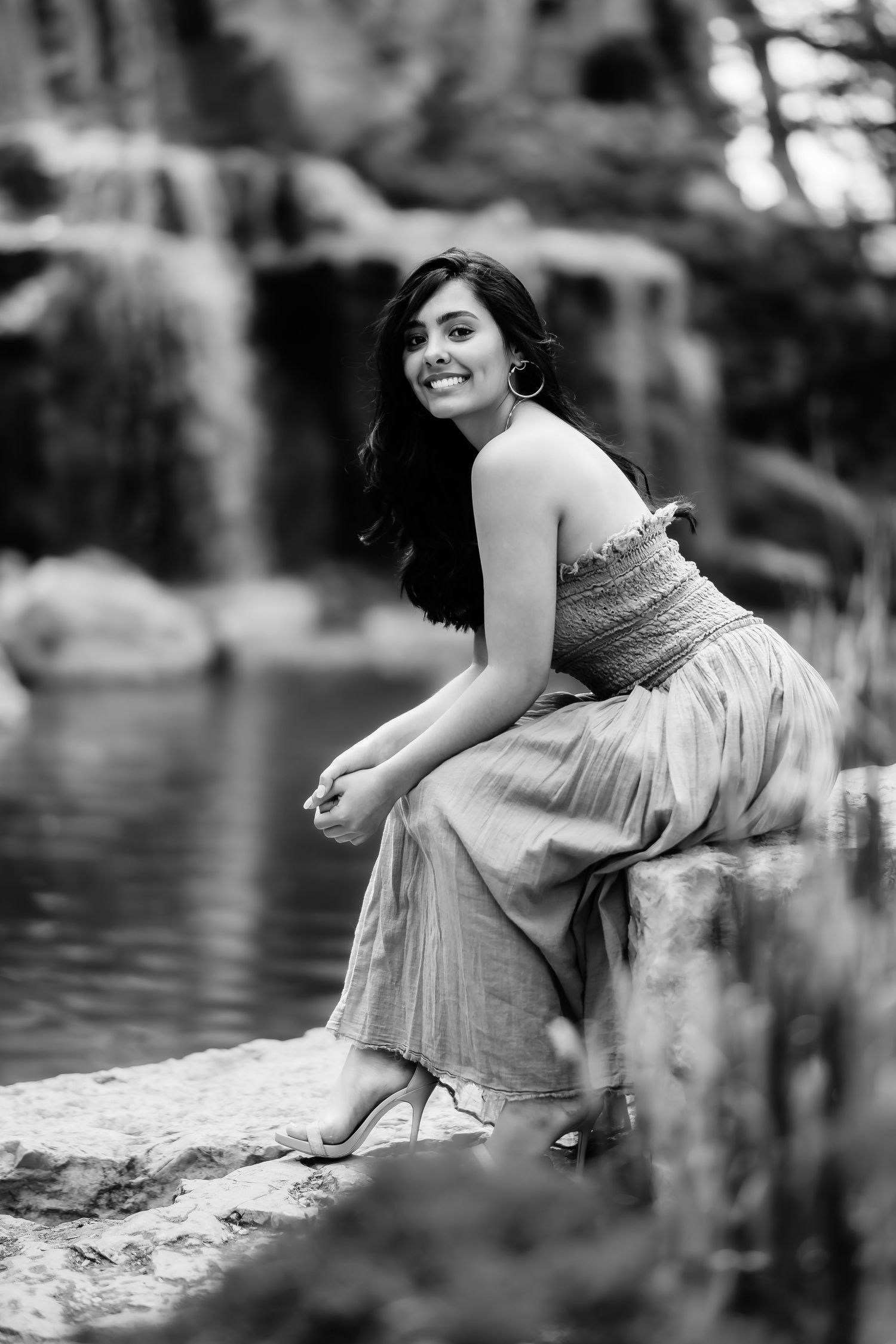 A black and white photo of a person sitting by a waterfall.
