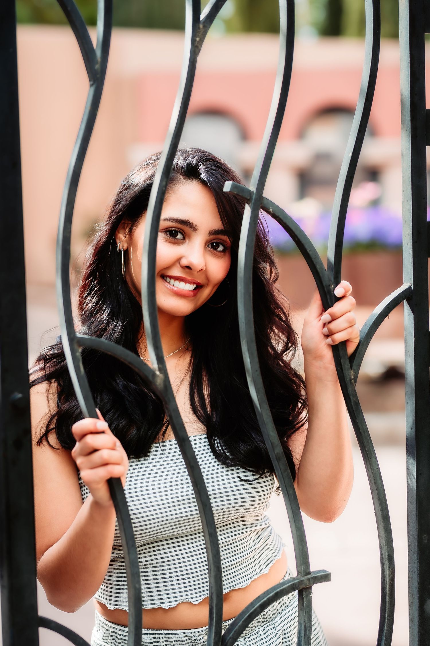 Playful portrait through decorative iron gates showing someone smiling and holding the bars.