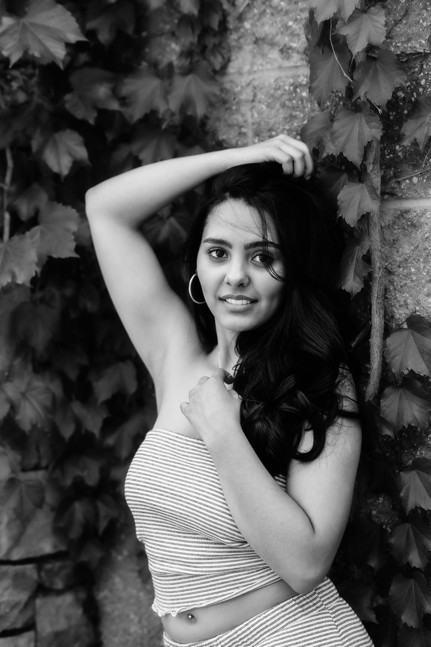 Black and white portrait of woman in striped top against ivy wall.