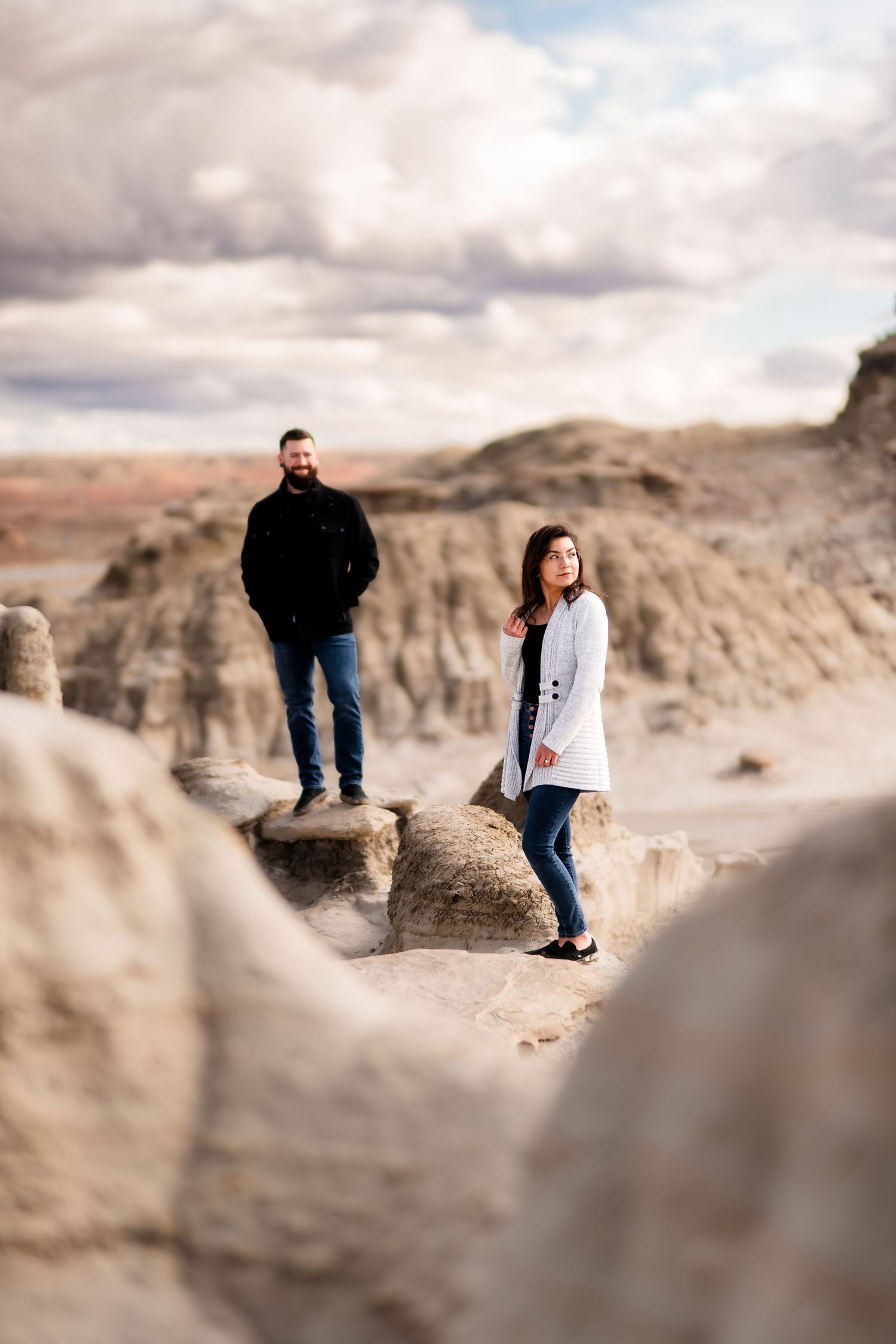 Two people stand apart on rocky desert terrain under dramatic cloudy skies.