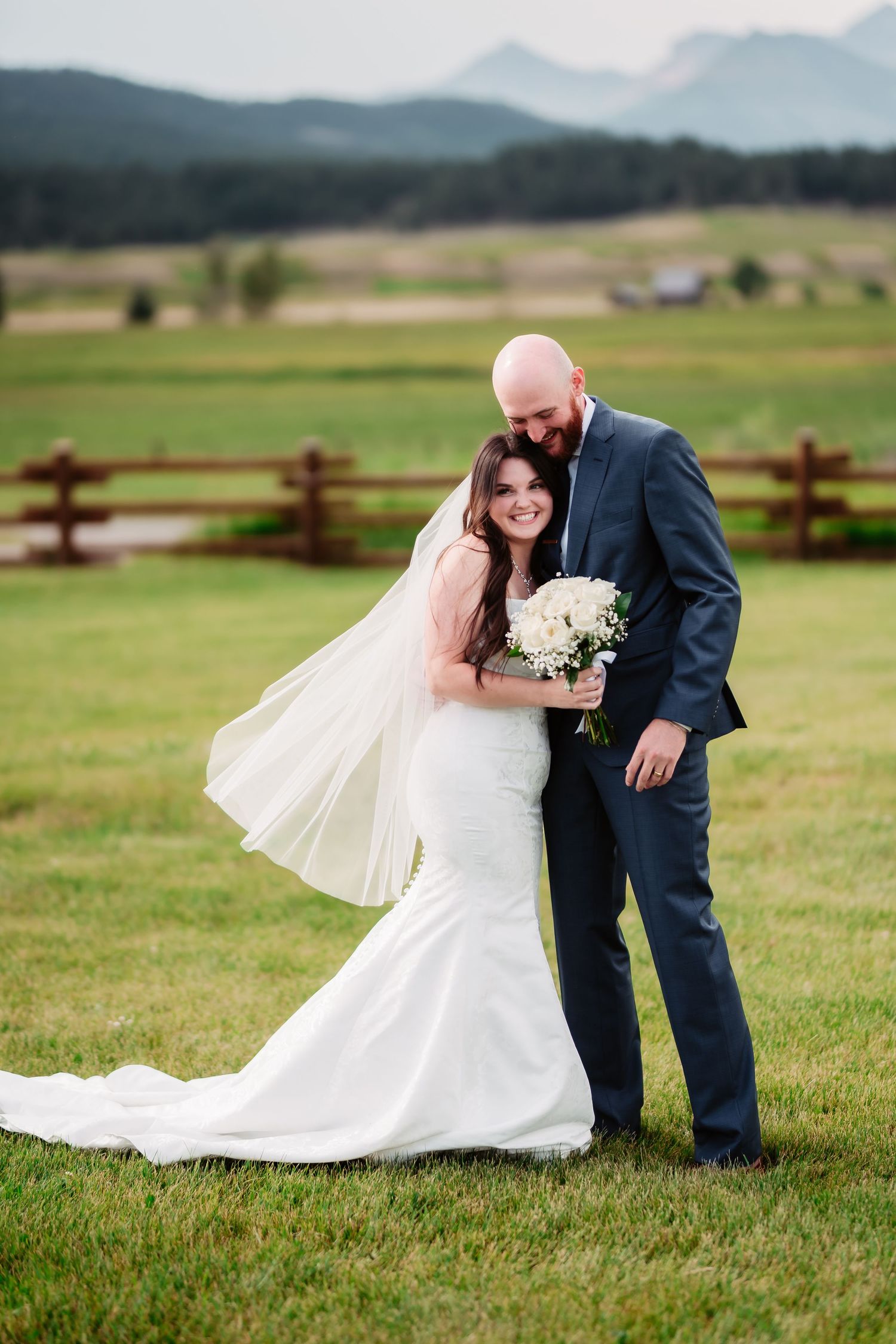 A romantic wedding portrait in a scenic mountain meadow with rustic fencing.