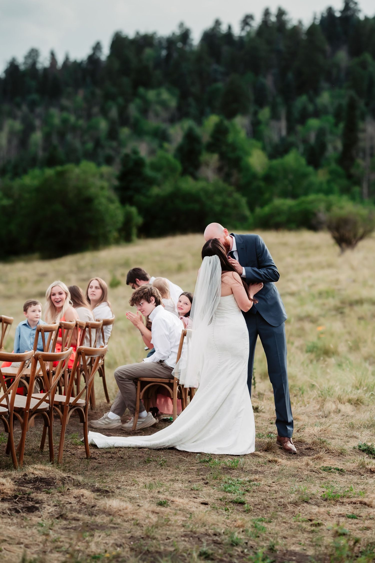 Wedding ceremony setup on grassy hillside with wooden chairs and mountain scenery.