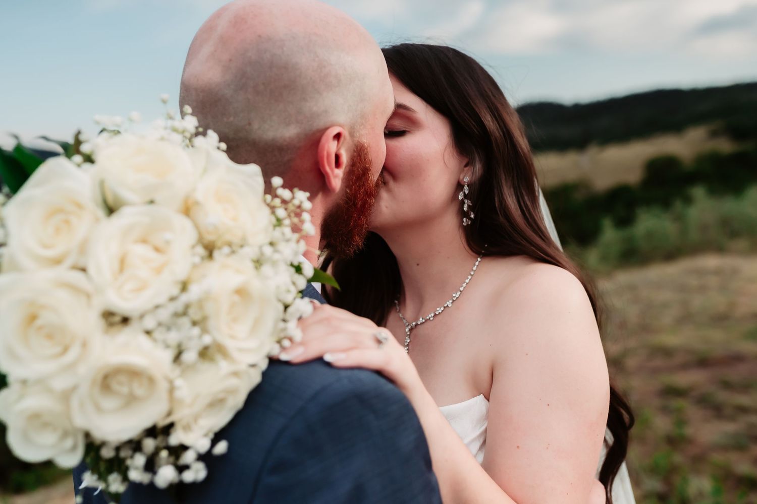 An intimate wedding moment with white roses and mountains creating a romantic backdrop.