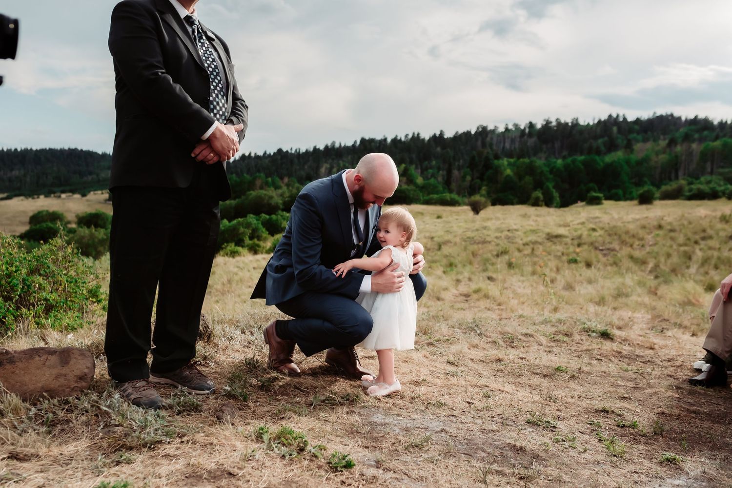 Wedding ceremony moment captured in scenic mountain meadow with pine forests in background.