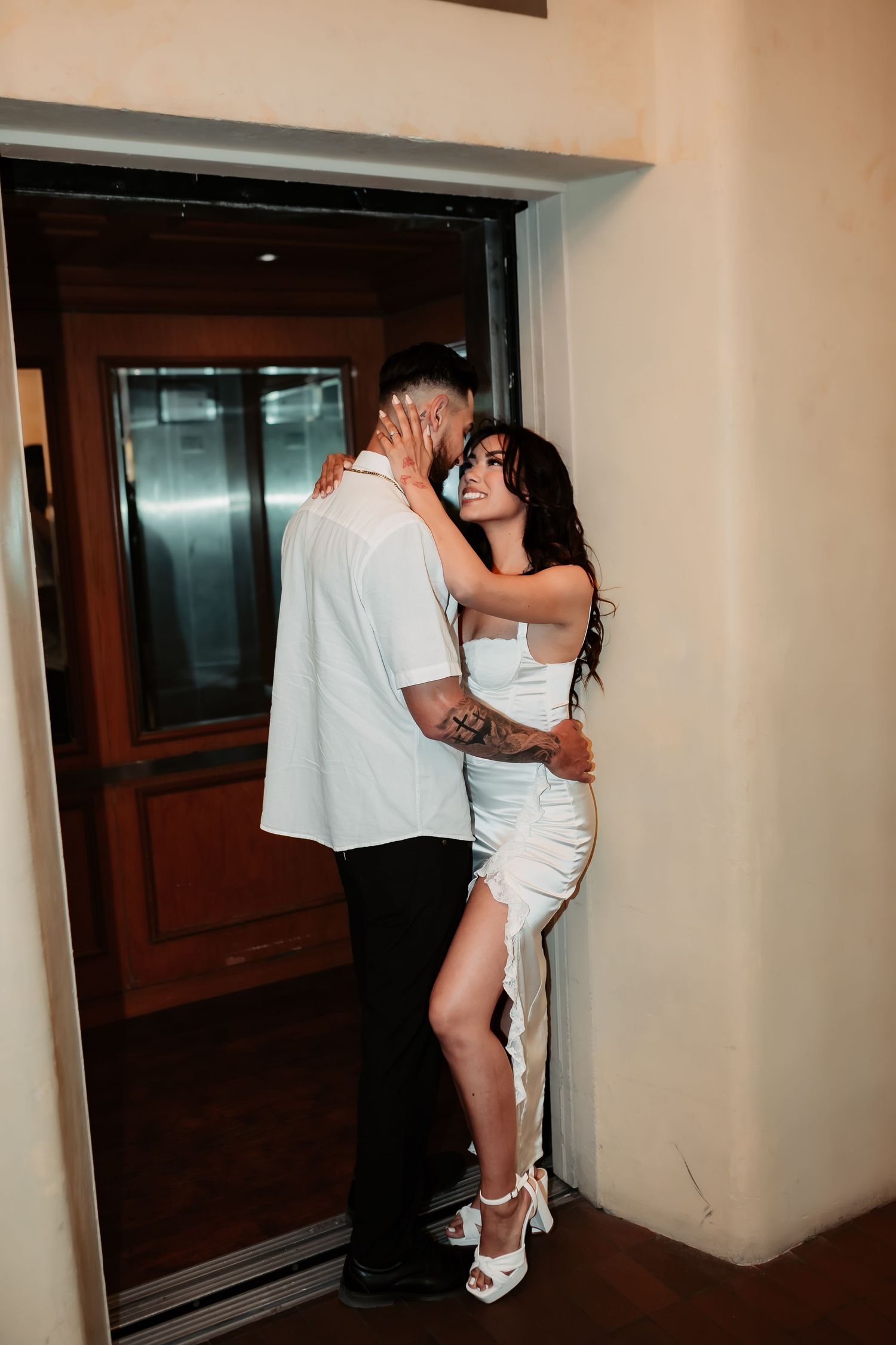 Couple embracing passionately in a dimly lit hallway by elevator entrance.