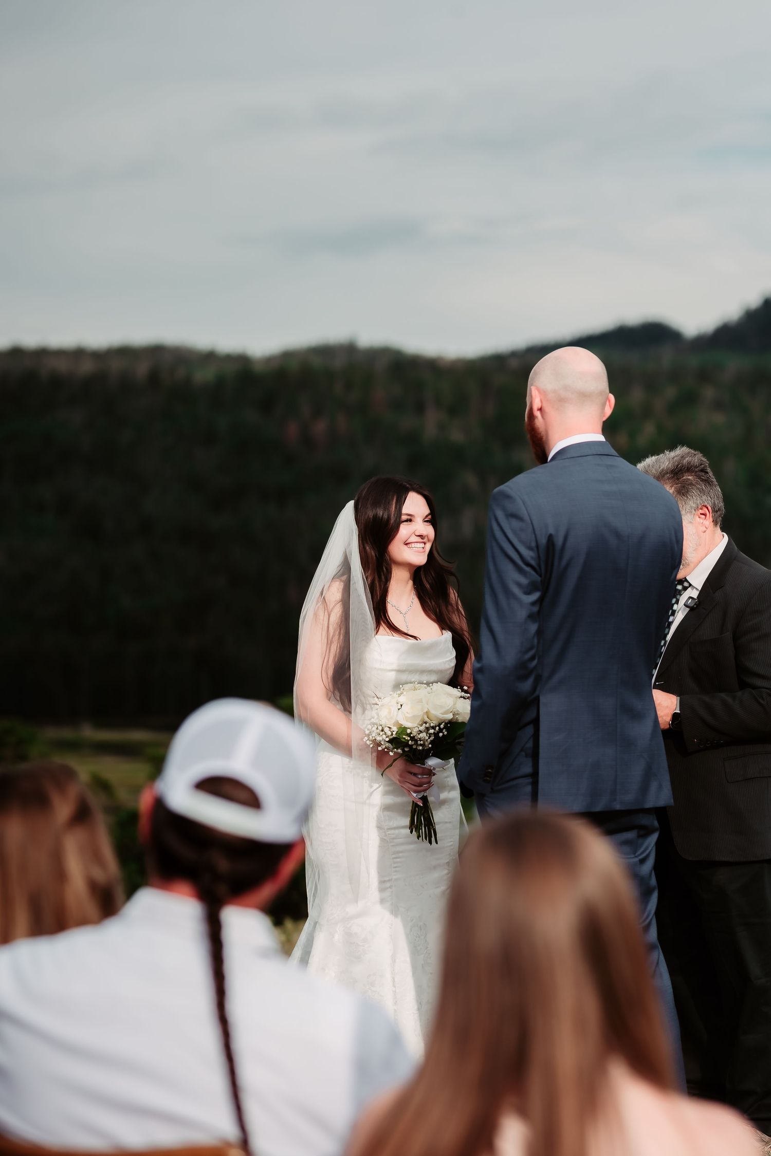 Outdoor mountain wedding ceremony with bride holding white bouquet.