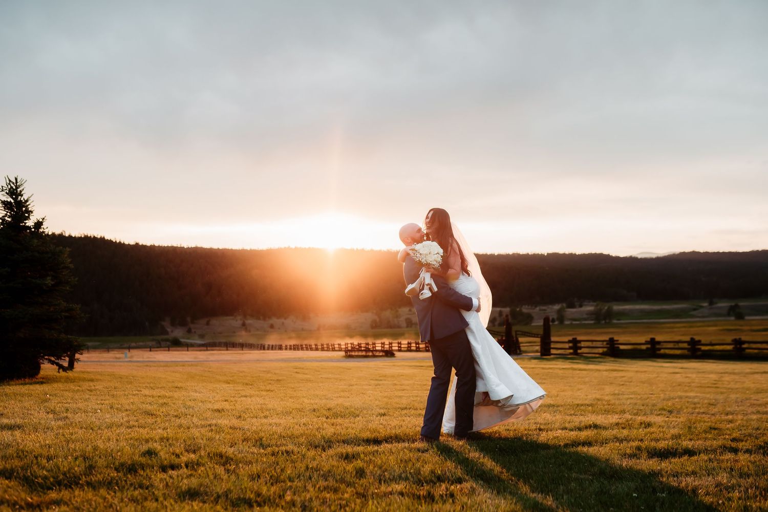 Newlyweds dance across field bathed in warm sunset light.