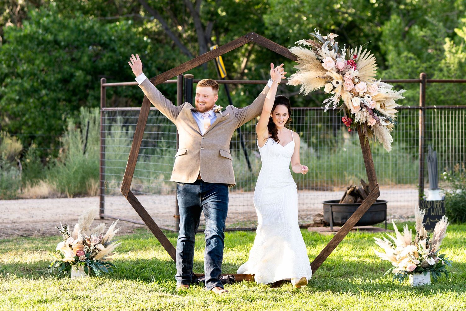 A celebratory moment with raised arms under a wooden arch decorated with dried floral arrangements.
