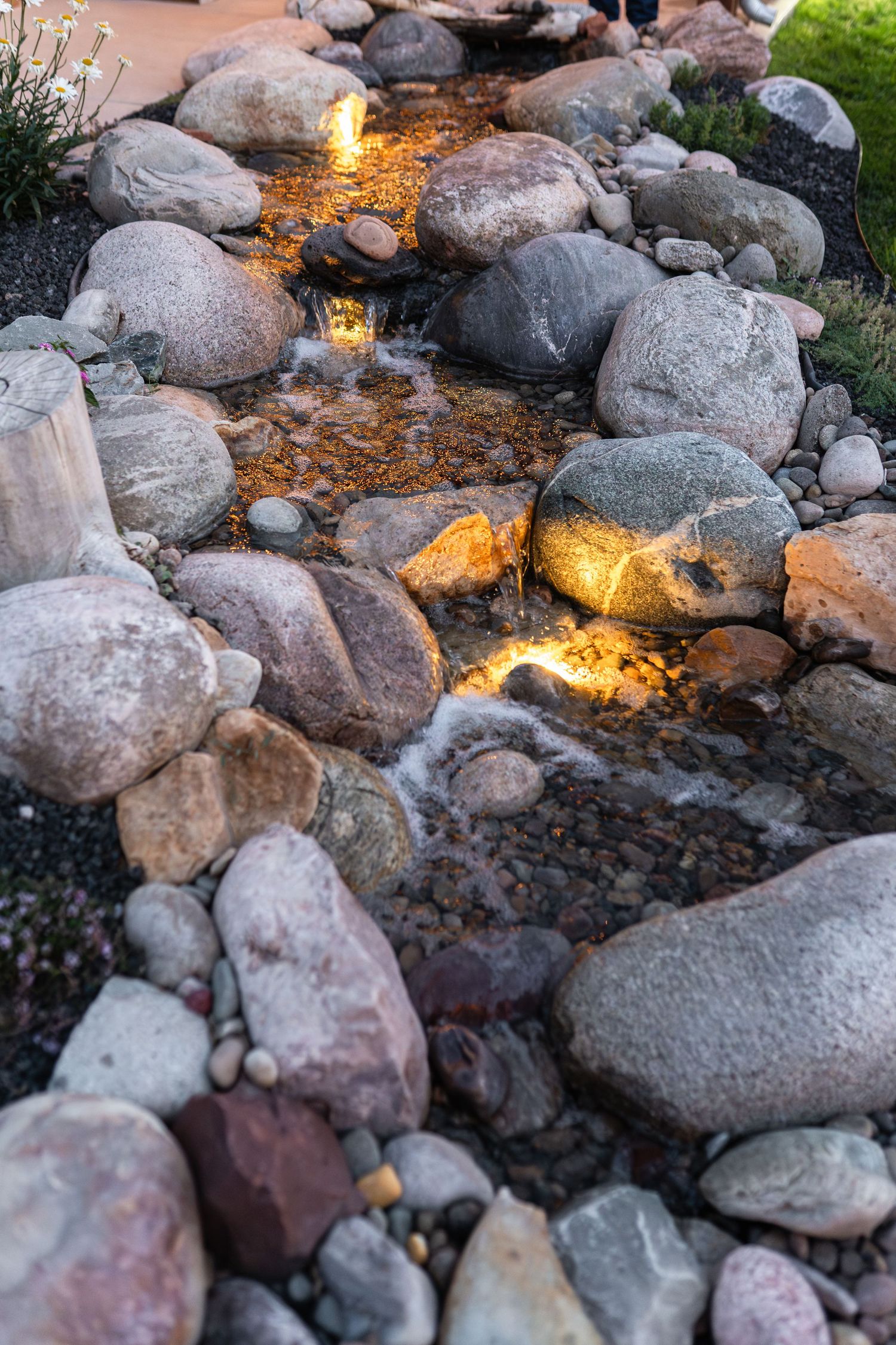 Illuminated rock water feature with glowing lights highlighting the flowing water between natural stones.