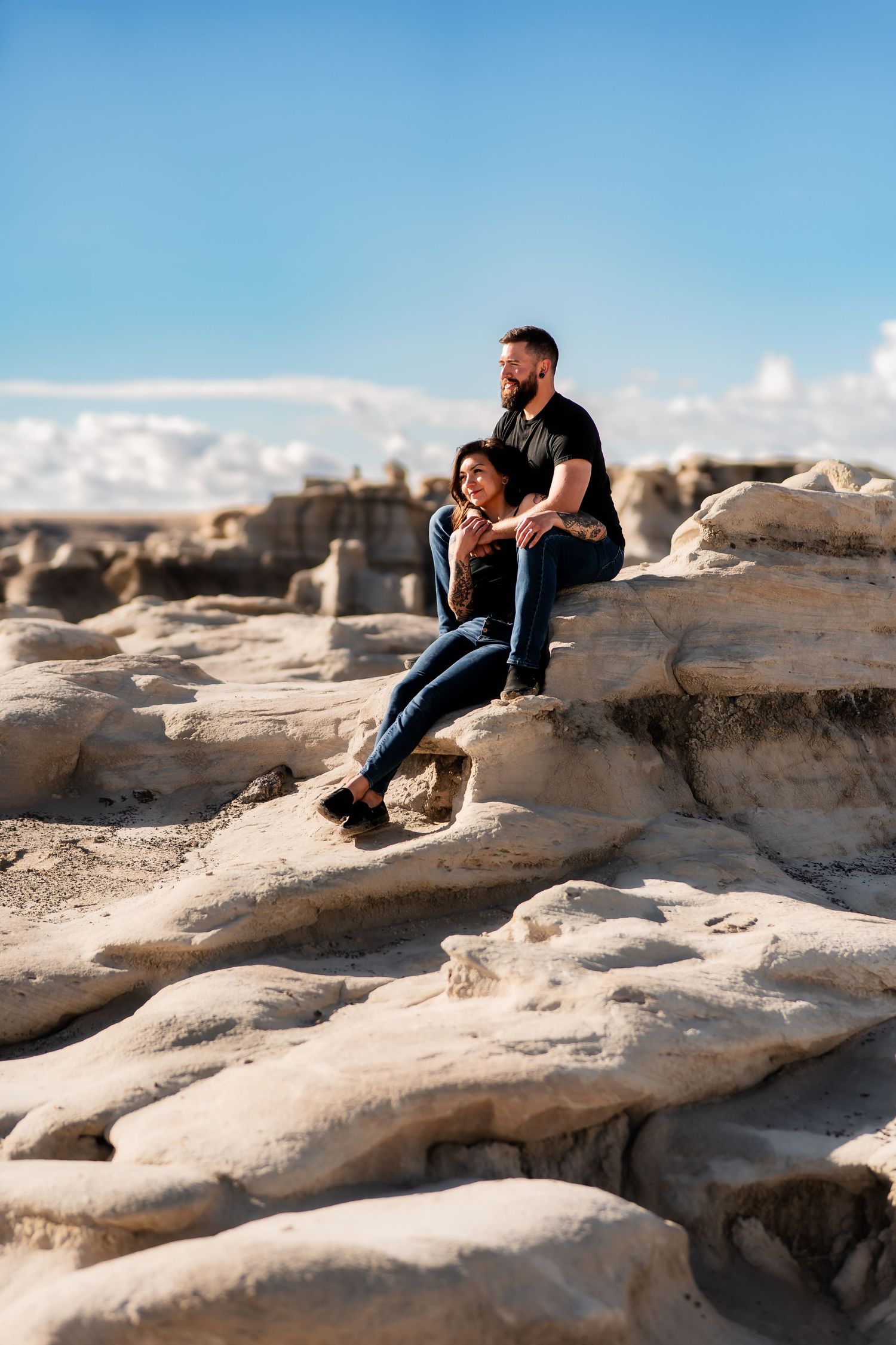 Couple sitting together on unique desert rock formations under bright blue sky.