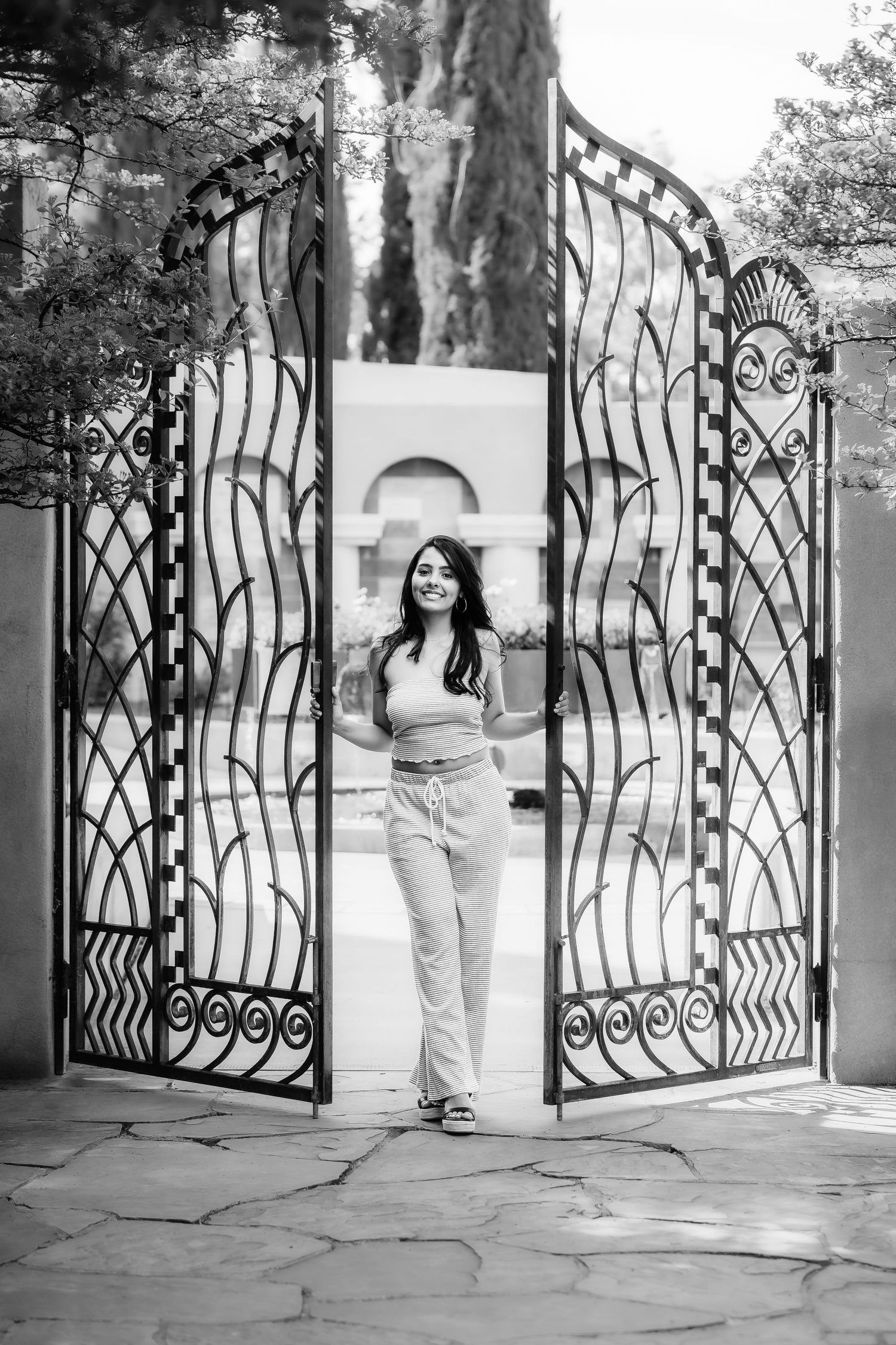 A black and white photo of someone standing between ornate wrought iron gates.