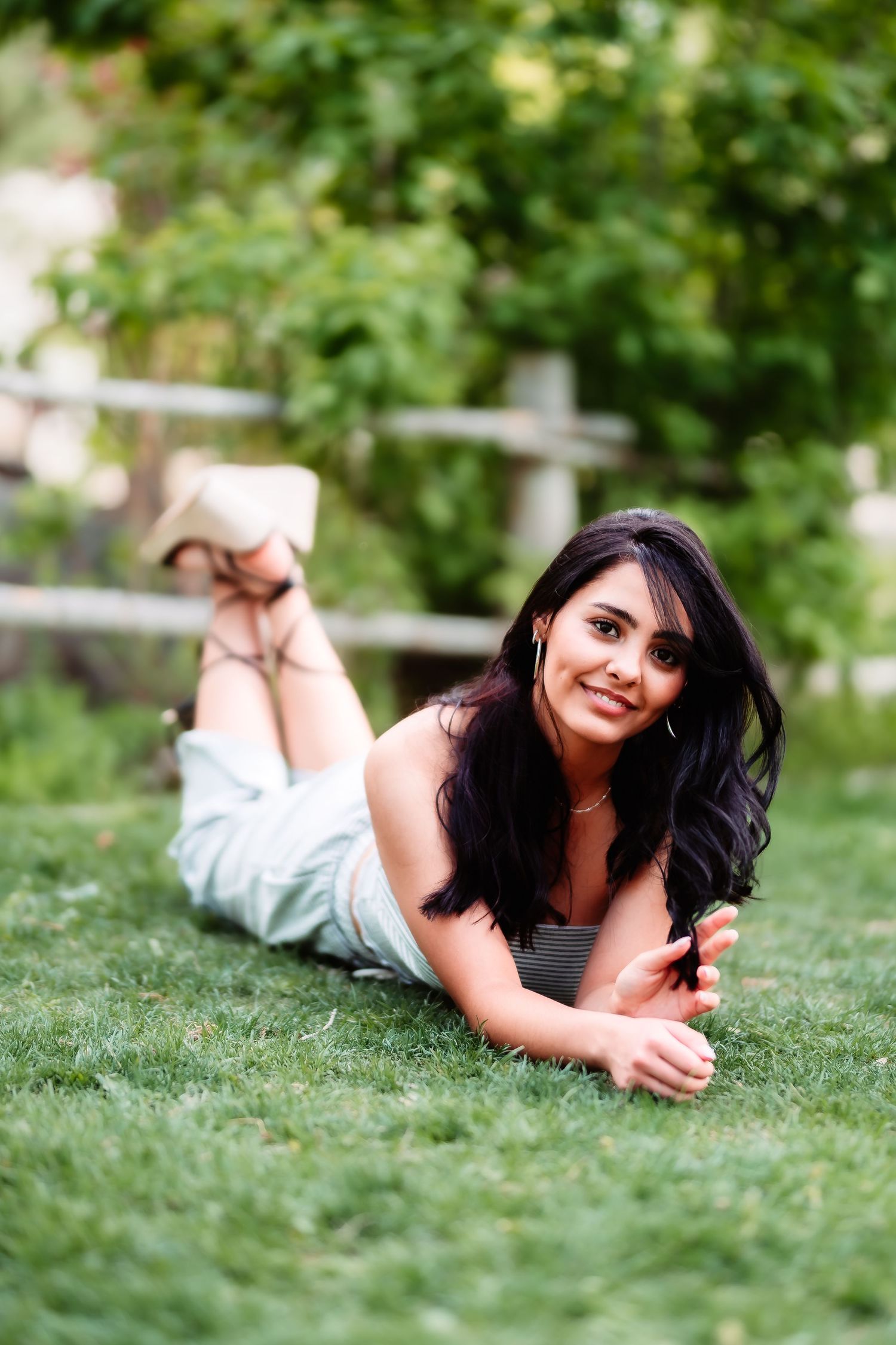 A casual outdoor portrait shows someone lying on green grass in a relaxed pose with long dark hair.