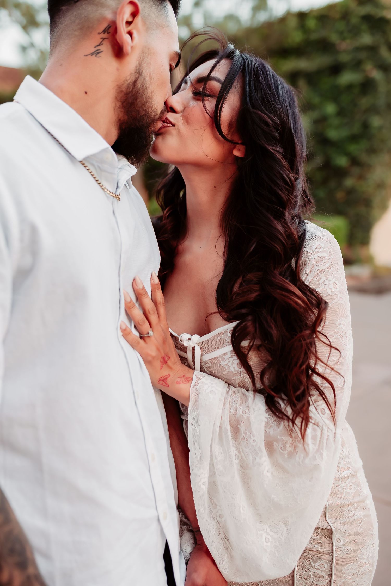 Romantic couple sharing an intimate kiss outdoors, with the woman wearing a white lace top.