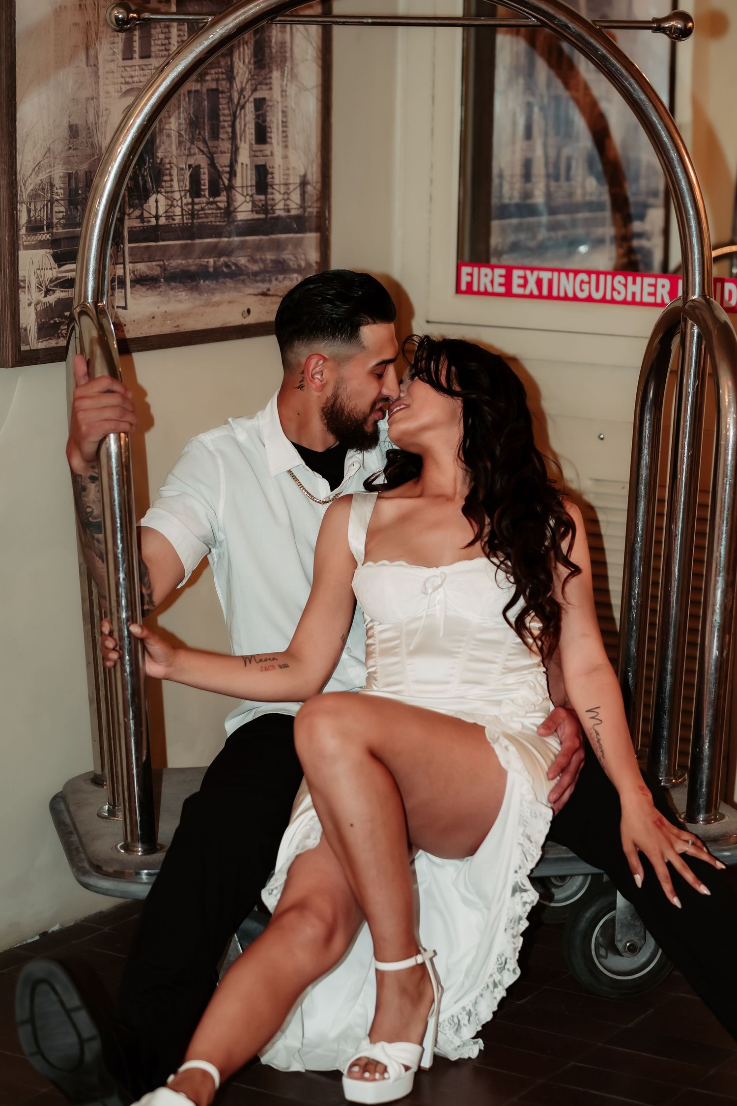 Intimate couple's portrait on a hotel luggage cart with artistic lighting.
