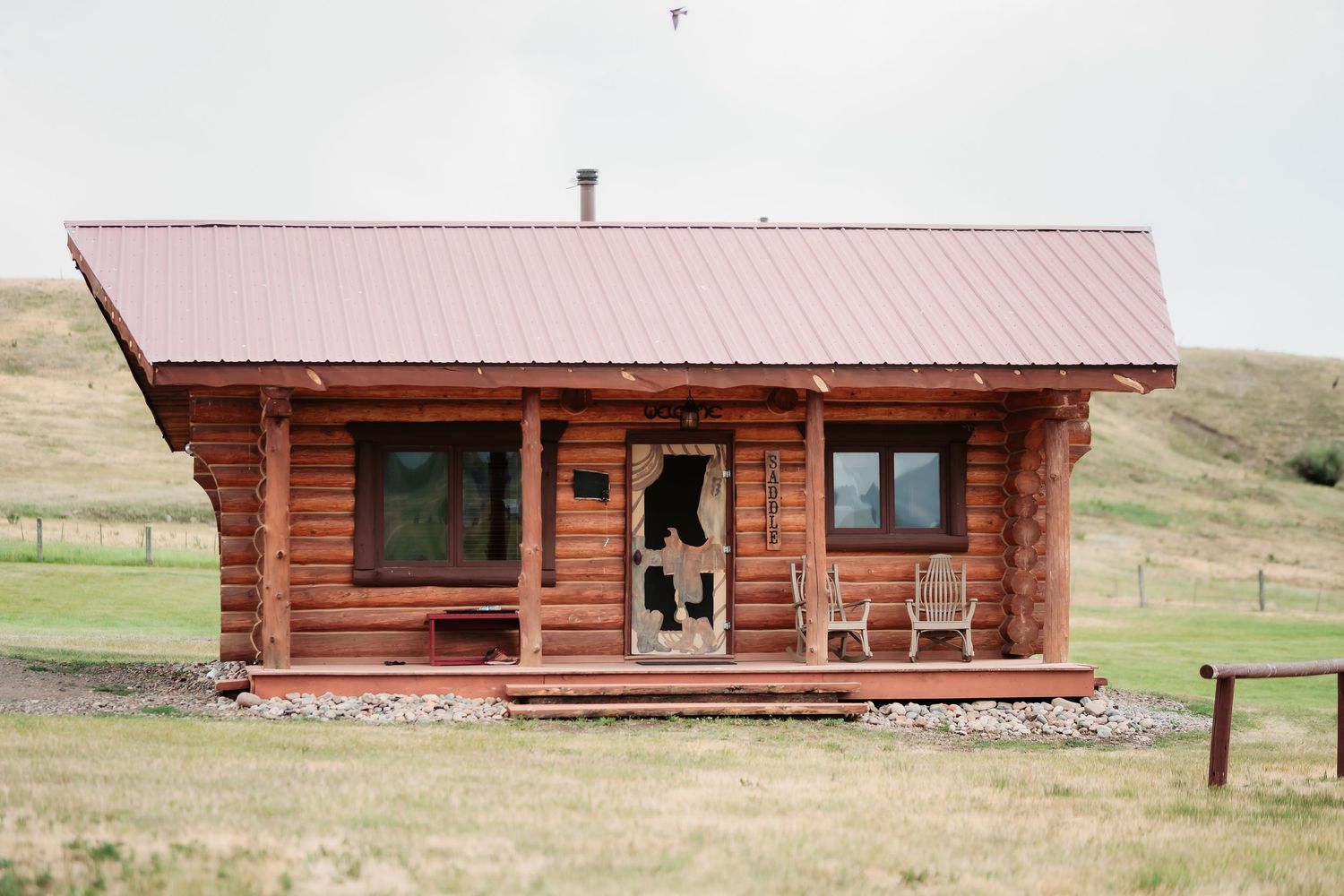 Panoramic view of rustic log cabins with red roofs against rolling hills and mountain landscape.