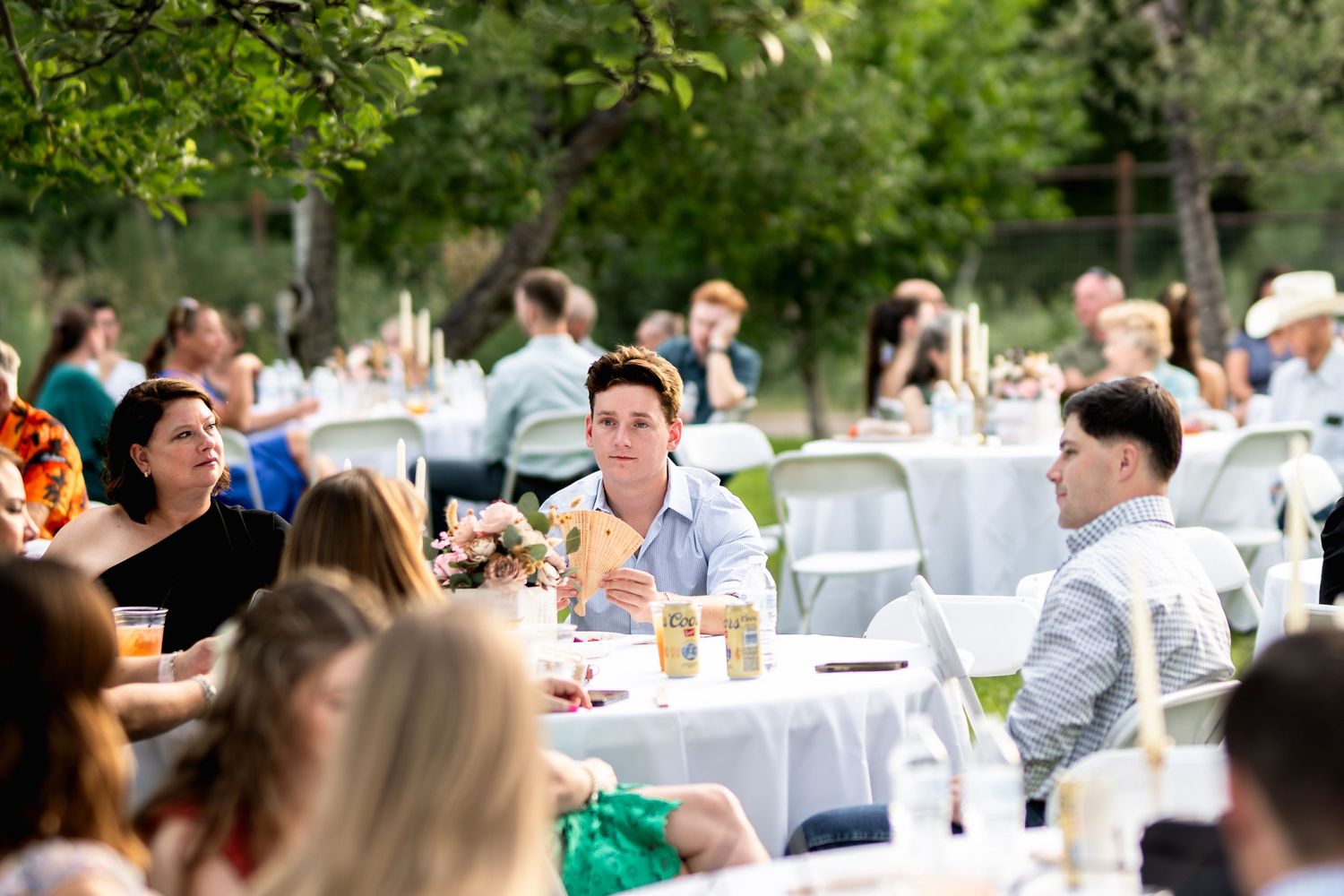 Outdoor wedding reception with guests seated at decorated tables under trees.