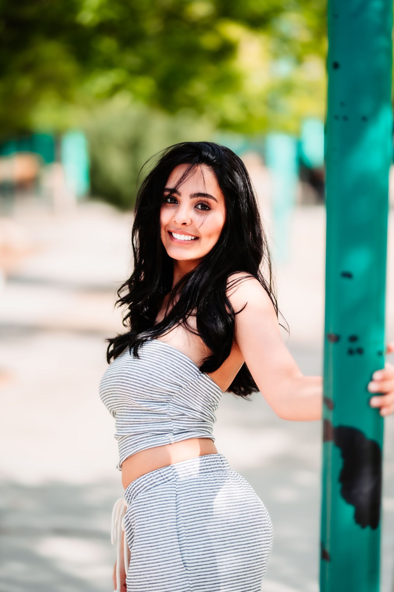 Athletic pose in grey striped activewear next to a turquoise pole outdoors.