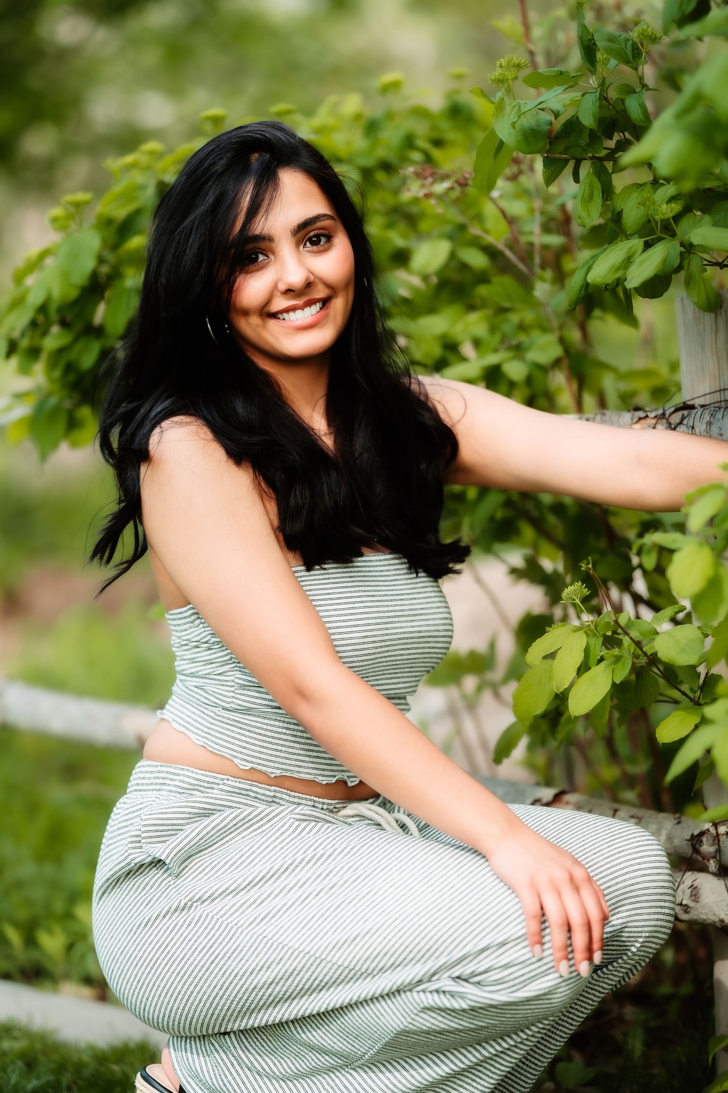 Relaxed summer portrait in a striped dress against garden foliage.