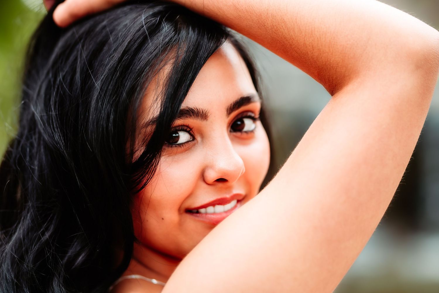 Close-up portrait with hand raised against natural outdoor background.