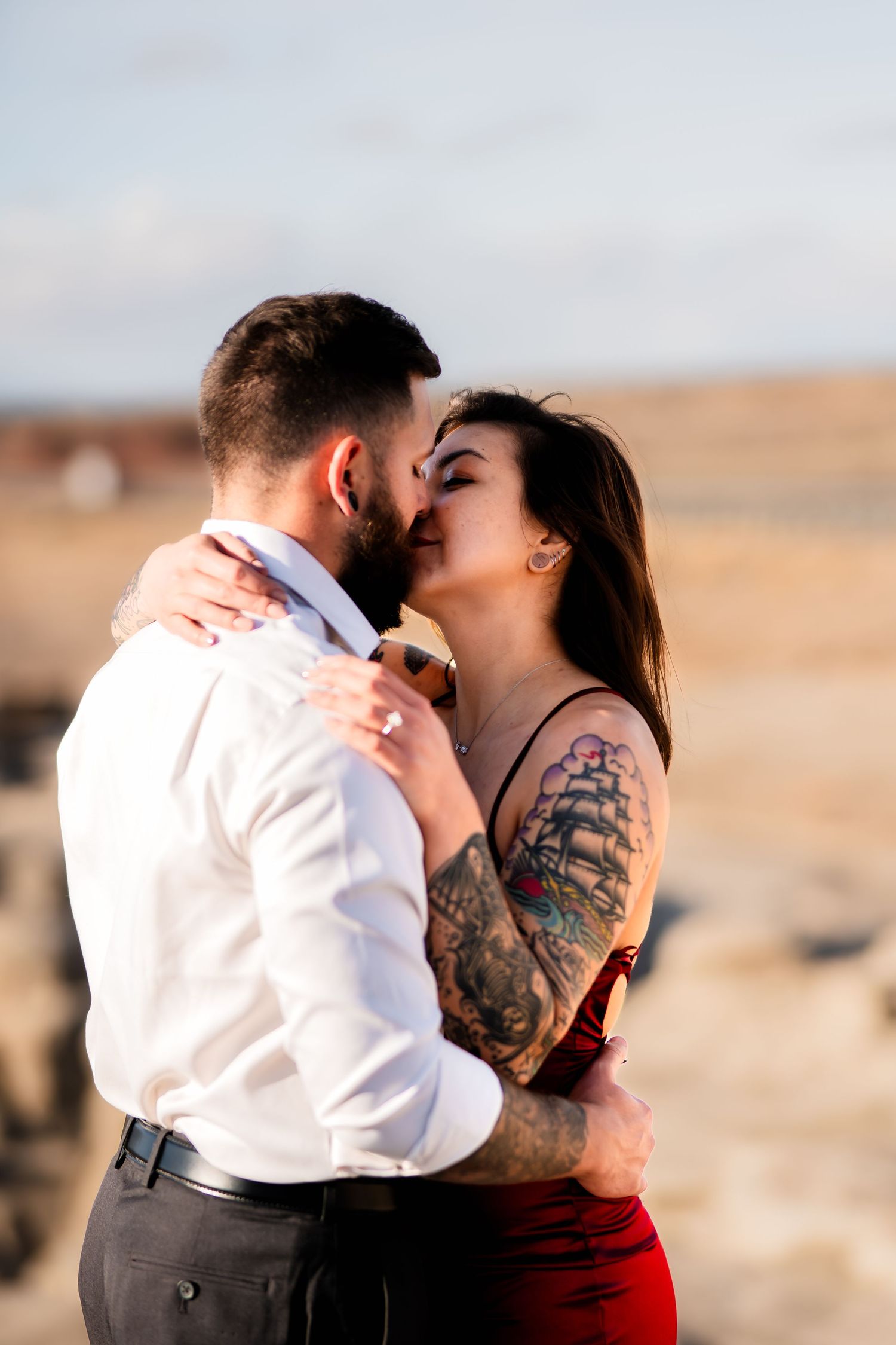 A couple embraces in formal attire against a desert backdrop at sunset.